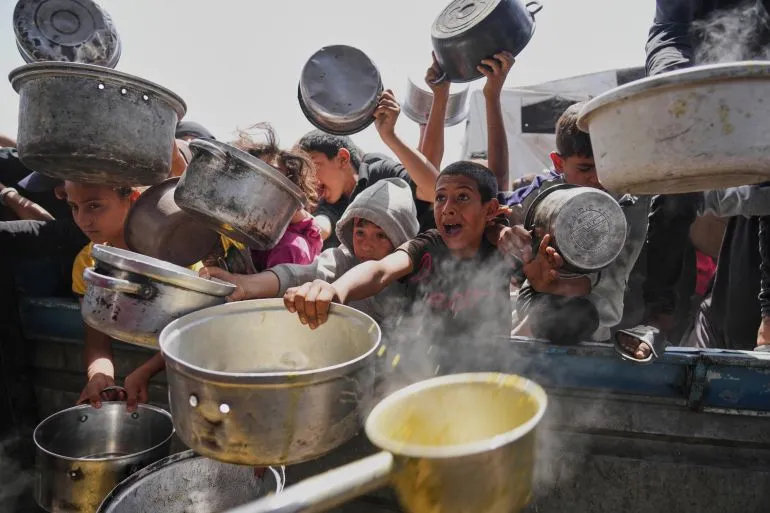 أطفال فلسطينيون في غزة يصطفون بحاويات فارغة للحصول على الطعام وسط أزمة المجاعة والحصار الإسرائيلي المستمر على القطاع.