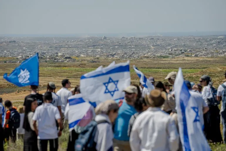 مستوطنون إسرائيليون يحملون أعلام إسرائيل في منطقة مفتوحة قرب غزة، في سياق خطط إقامة مستوطنات جديدة وسط تصاعد التوترات السياسية والأمنية.