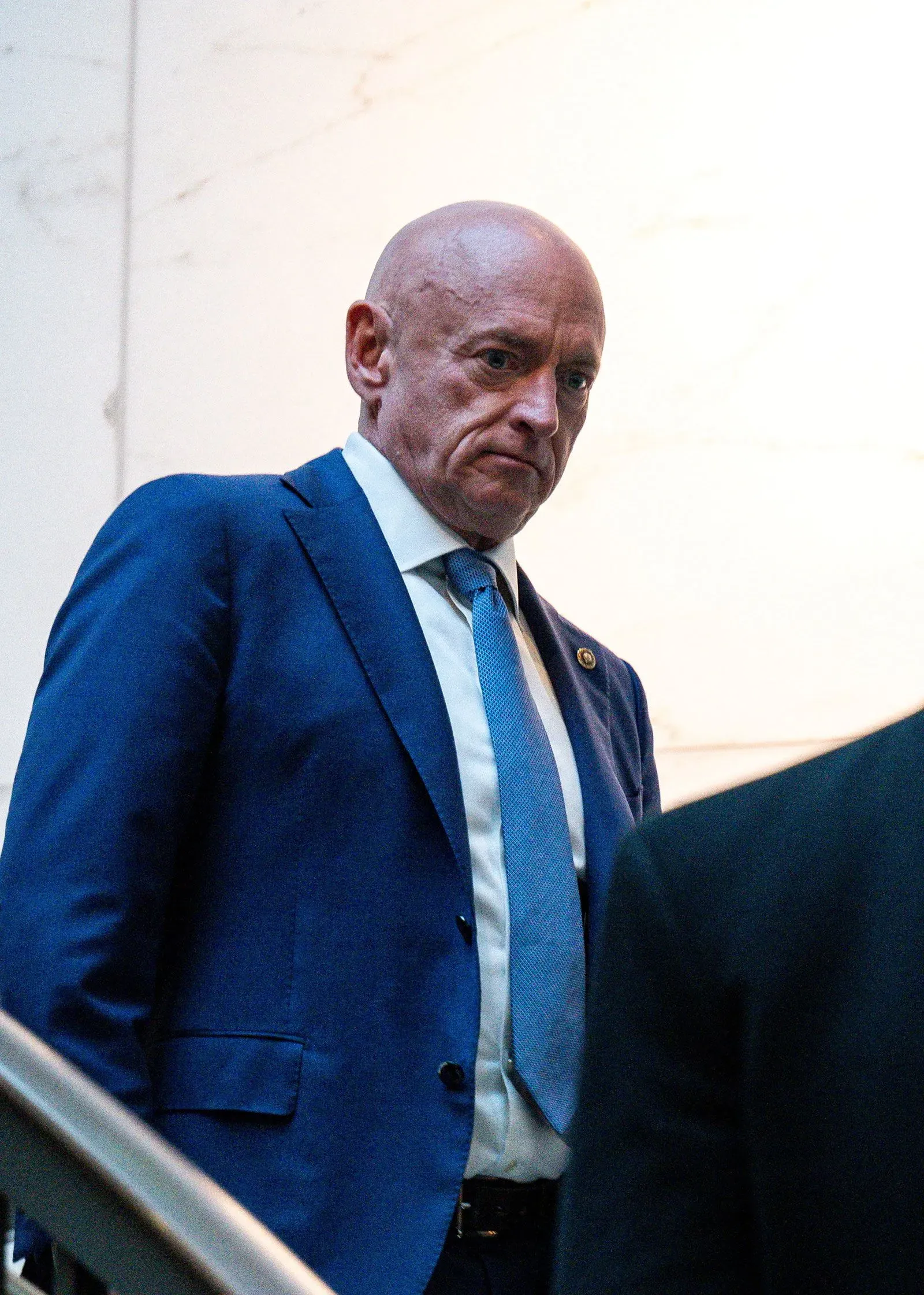 رجل يرتدي بدلة زرقاء وقميص أبيض، يبدو متجهم الوجه أثناء صعوده السلم، مما يعكس توتر الأجواء السياسية حول مسؤولية ترامب وإدارته.