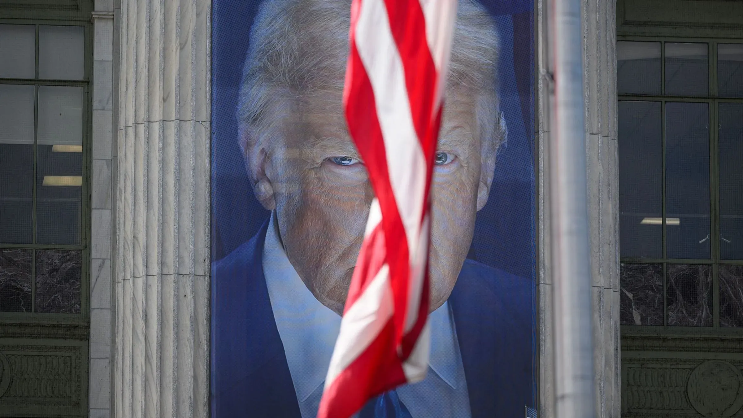 صورة تظهر وجه الرئيس السابق دونالد ترامب على لافتة كبيرة، مع العلم الأمريكي يتدلى بجانبه، مما يعكس الجدل حول المسؤولية القانونية في إدارته.