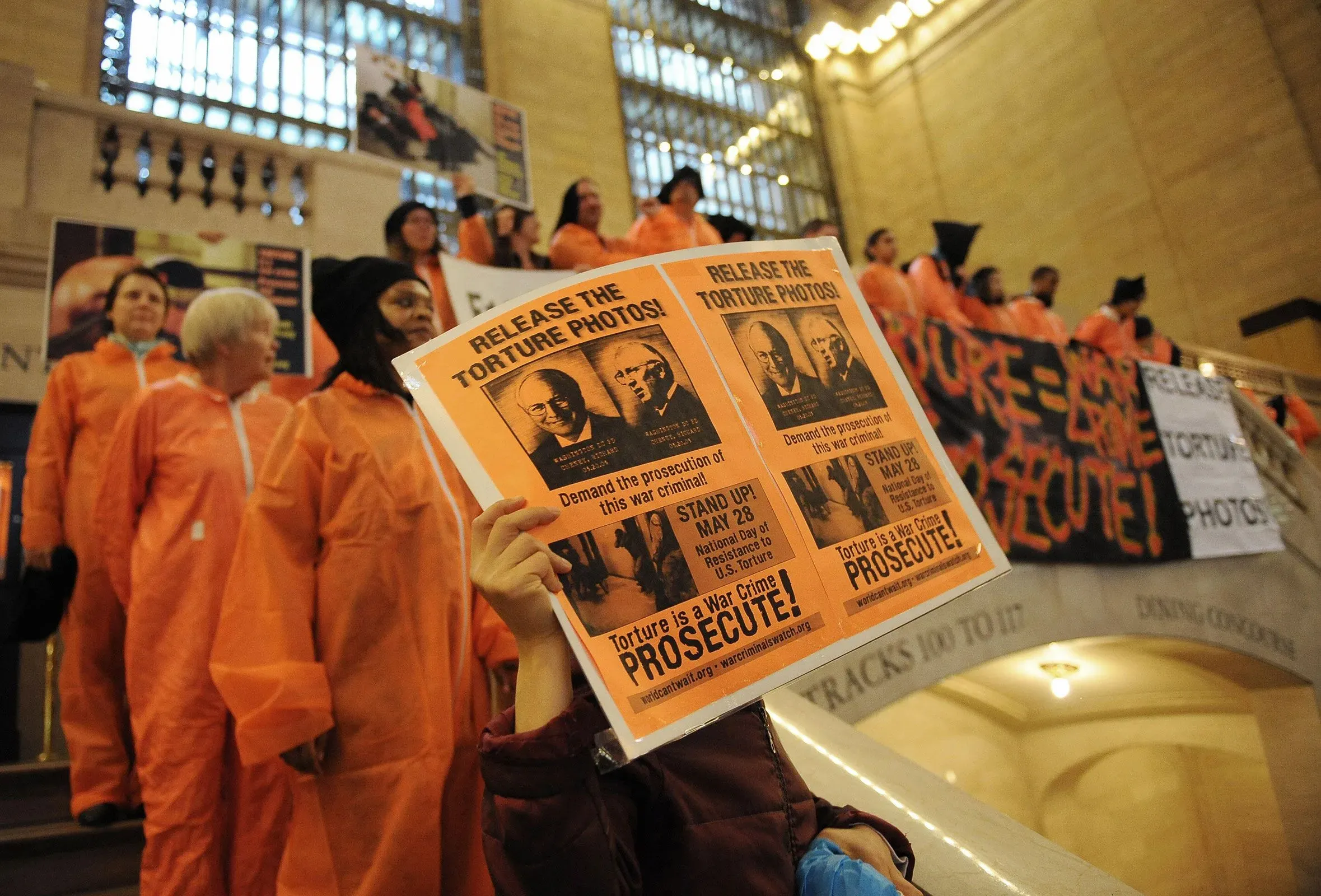 محتجون يرتدون زي البرتقالي يحملون لافتات تطالب بإطلاق صور التعذيب، مع التركيز على المساءلة عن الجرائم ضد الإنسانية.