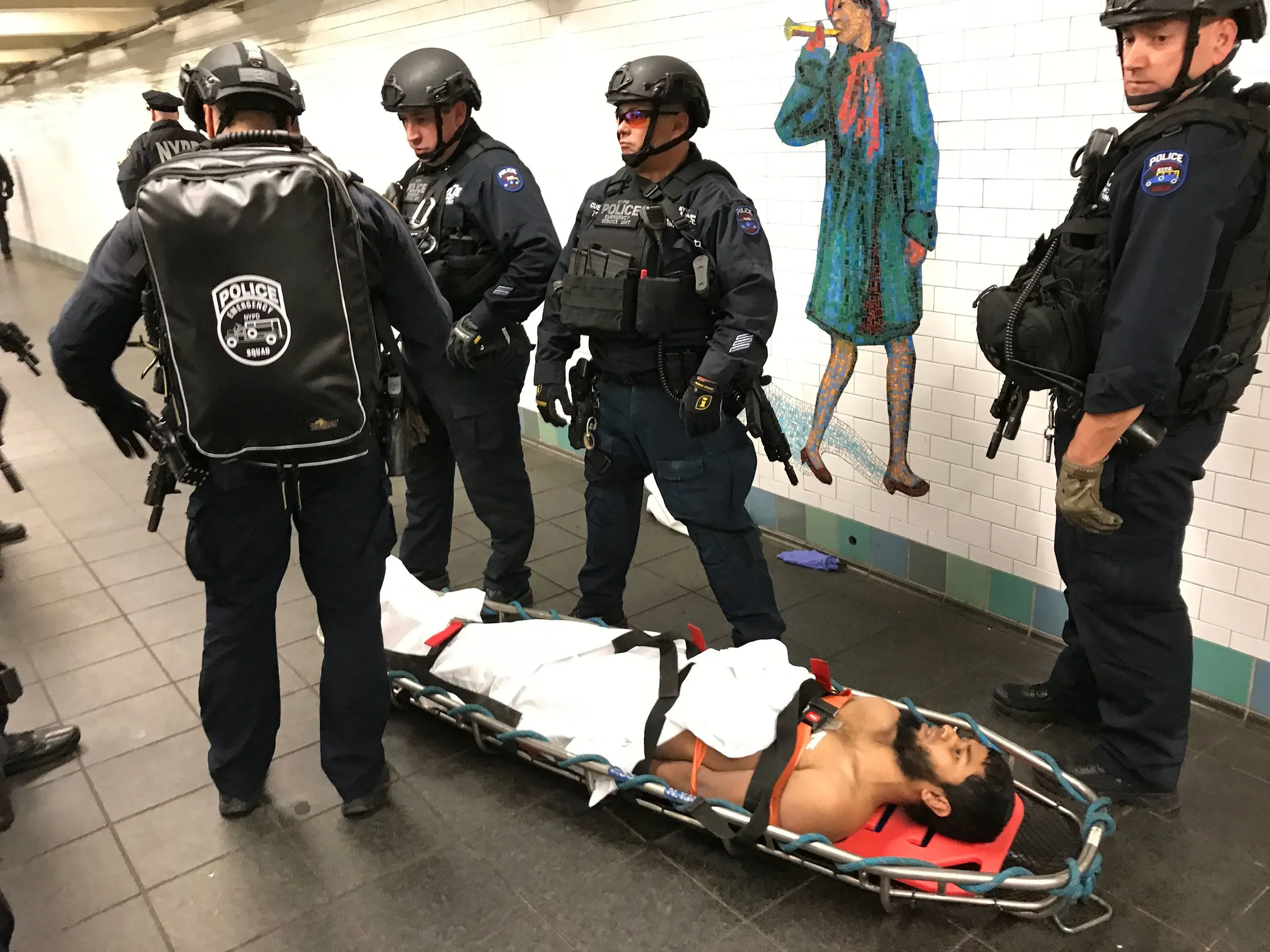 إجراءات الشرطة بعد انفجار قنبلة أنبوبية في محطة مترو نيويورك، مع وجود مشتبه به على نقالة وسط عناصر الأمن.