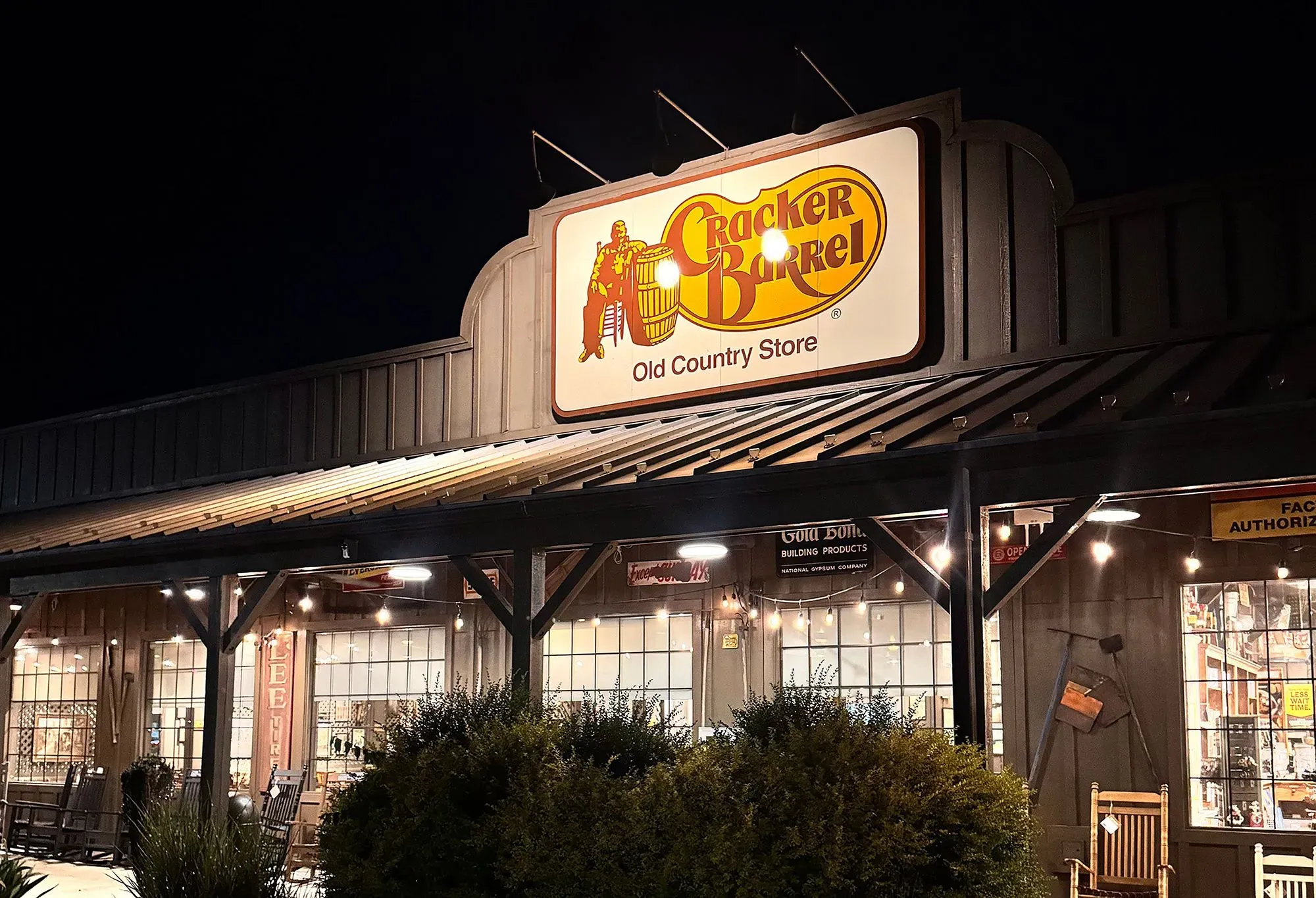 شعار كراكر باريل القديم يضيء على واجهة المتجر، وسط أجواء ريفية، مما يعكس تراث السلسلة وسط التغييرات الحديثة.