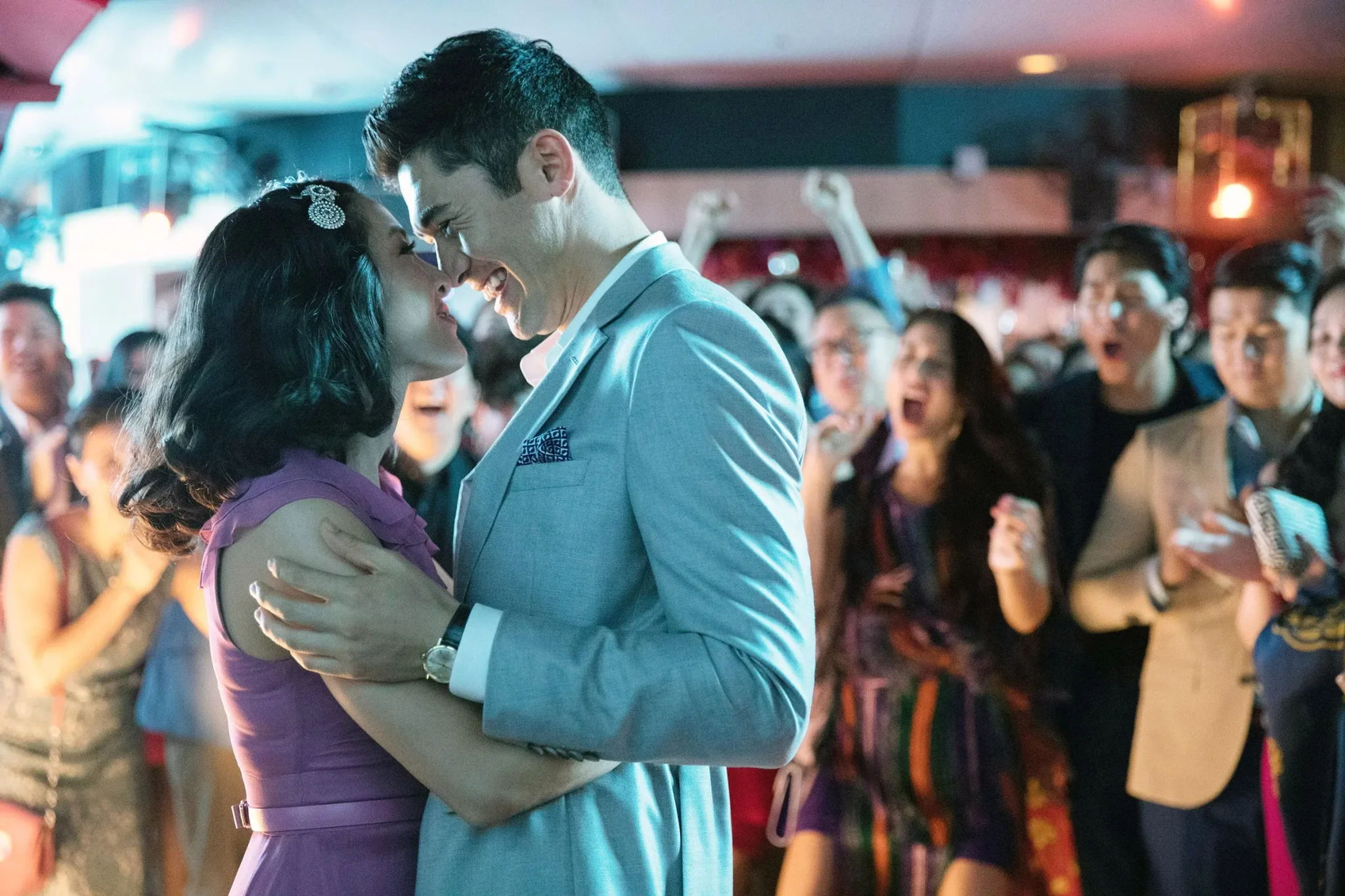 مشهد رومانسي من فيلم "Crazy Rich Asians" يظهر ريتشل ونيكولاس يرقصان وسط حشد يحتفل بزفاف، مع التركيز على الفخامة والثراء الآسيوي.