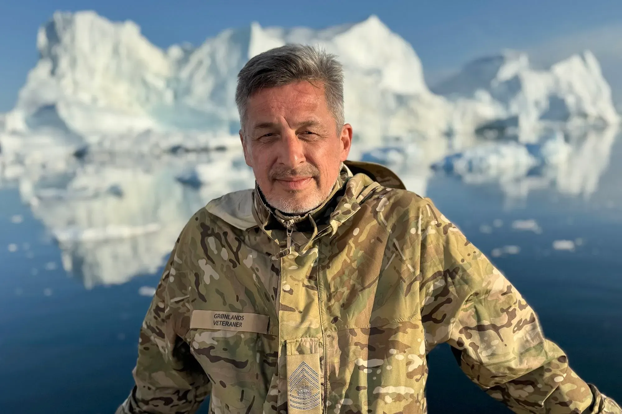 محارب دنماركي قديم يرتدي زيًا عسكريًا، يقف أمام مناظر جليدية في غرينلاند، معبرًا عن مشاعر الخيانة تجاه سلوك الولايات المتحدة.