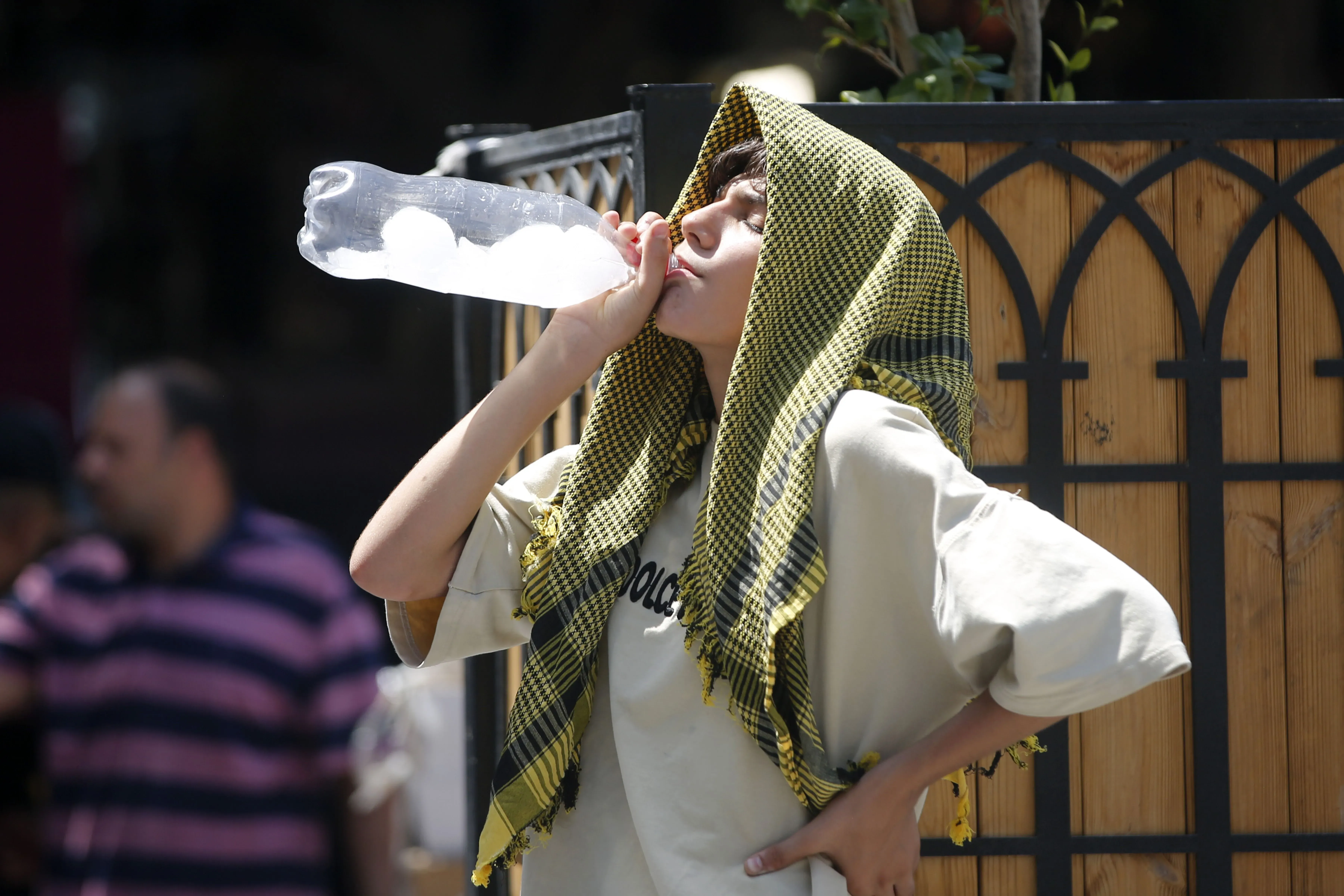 طفل يرتدي غطاء رأس، يشرب الماء من زجاجة كبيرة في طهران، حيث تعاني المدينة من أزمة مياه حادة وسط موجة حر شديدة.