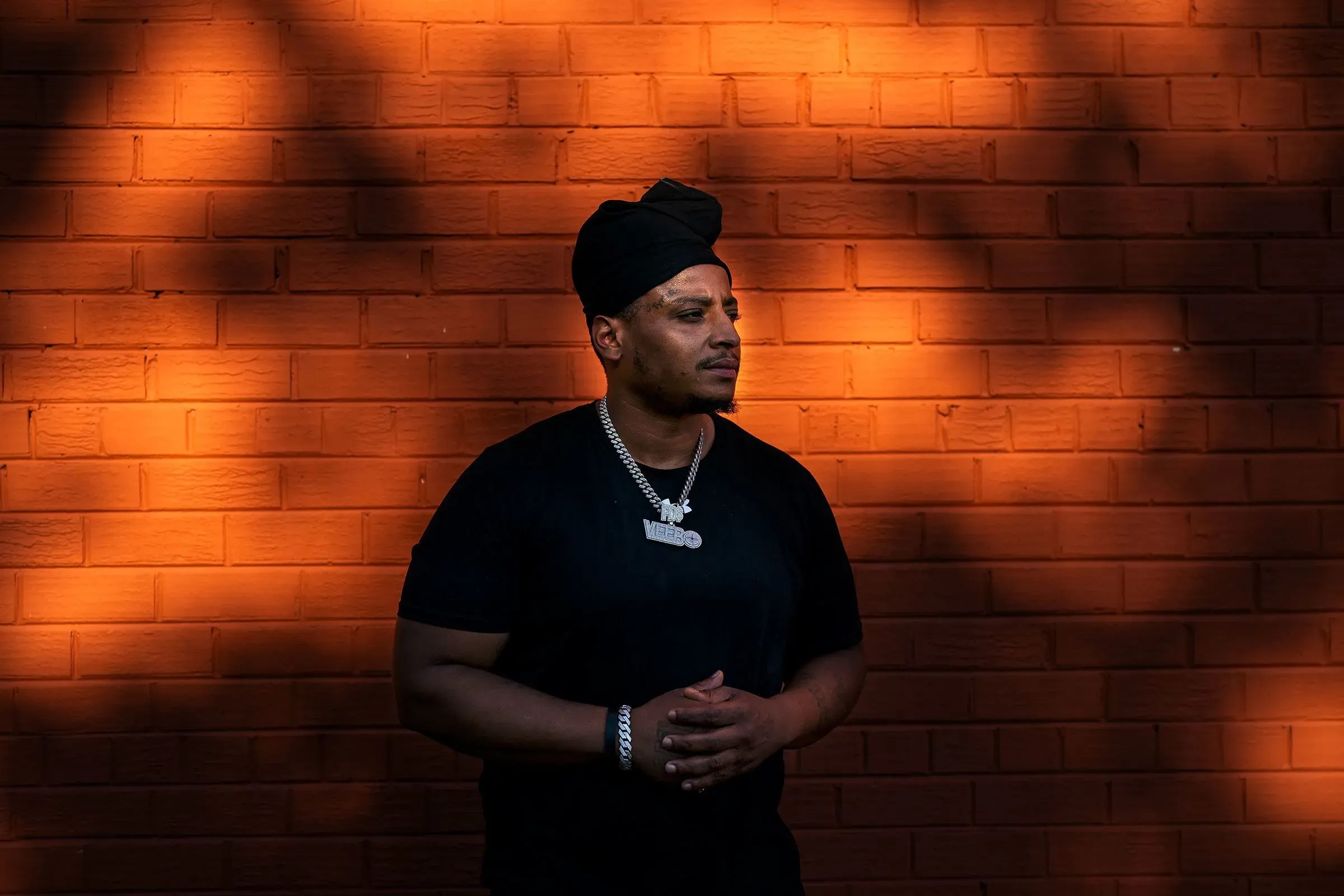 رجل يرتدي ملابس داكنة ويقف أمام جدار برتقالي، مع تعبير جاد، يعكس مشاعر القلق تجاه الوضع الأمني في مجتمعه.