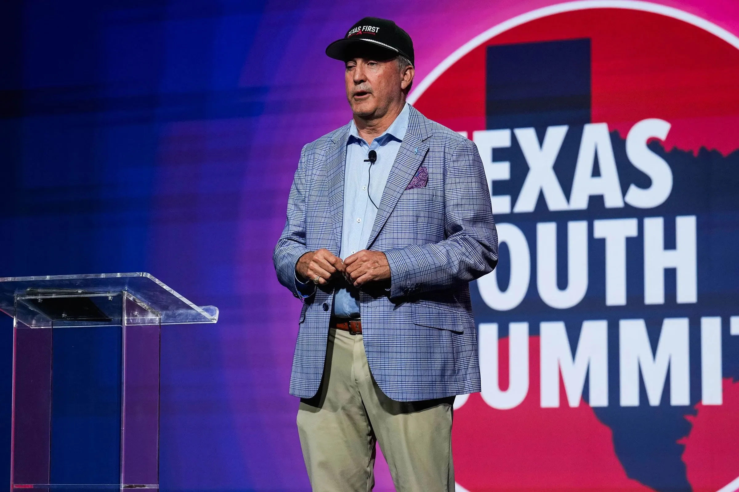 رجل يتحدث على منصة في قمة الشباب في تكساس، خلفه شعار الحدث. يتناول قضايا سياسية مهمة تتعلق بانتخابات مجلس الشيوخ.