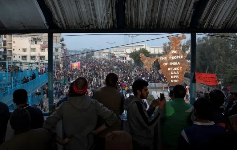 تظهر الصورة حشودًا كبيرة من المتظاهرين في نيودلهي، مع لافتة ضخمة تحمل عبارة "نحن شعب الهند نرفض CAA وNPR وNRC"، تعبيرًا عن الاحتجاجات ضد قانون الجنسية.