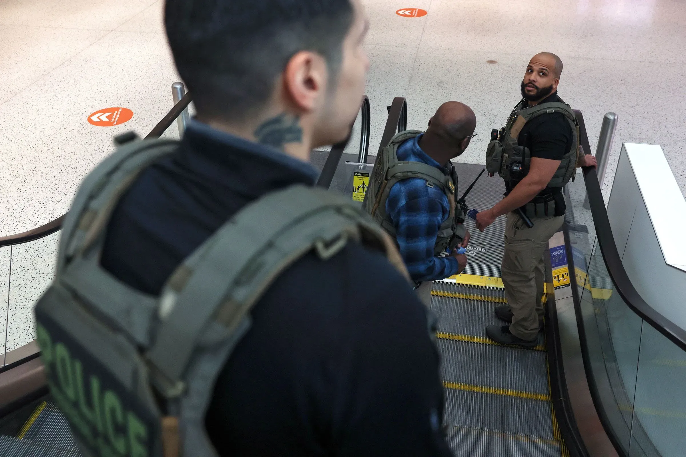 رجال أمن يرتدون زيًا رسميًا ومسلحين يتحدثون في منطقة مصعد، مما يبرز التوترات الأمنية المرتبطة بالانتخابات.