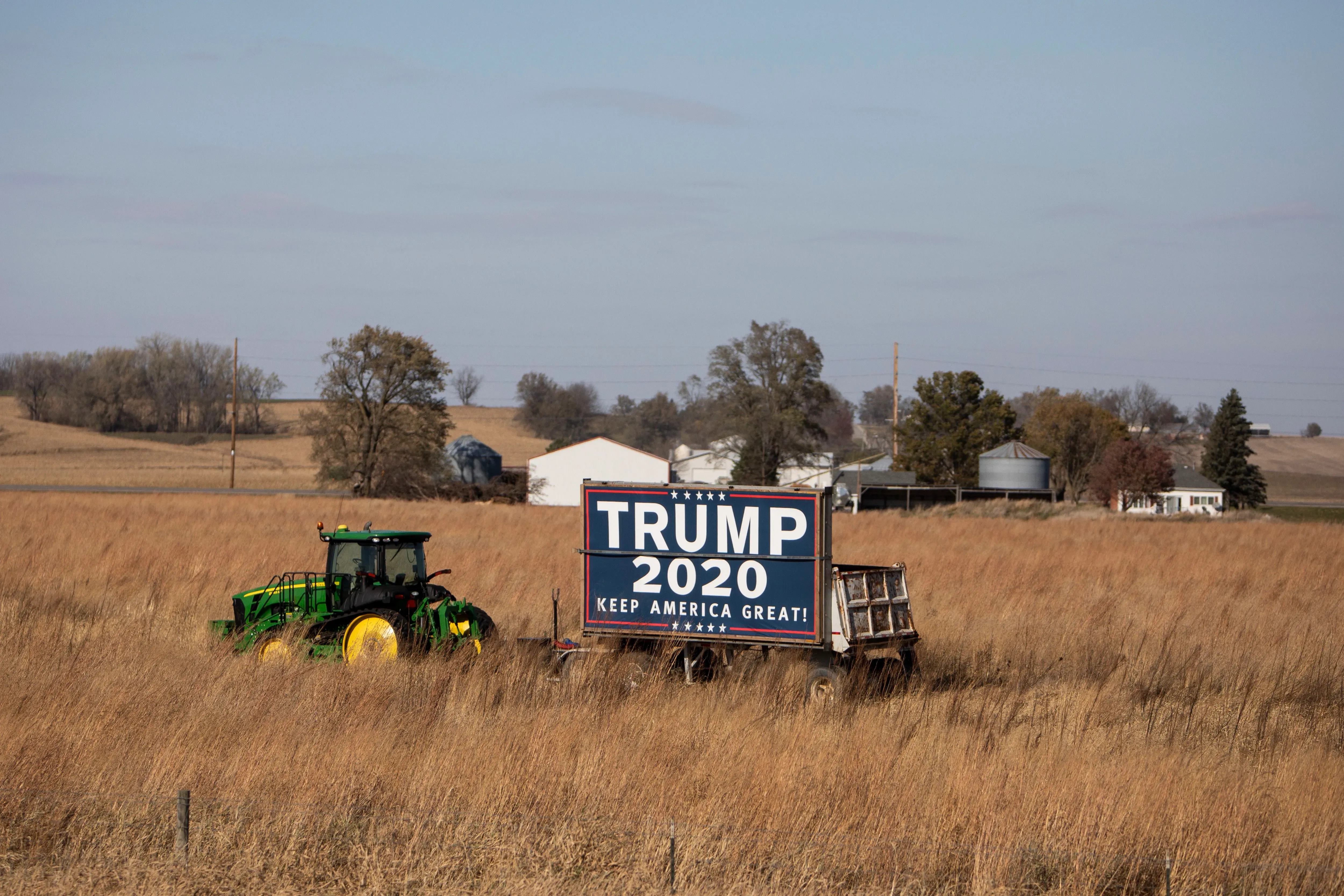لافتة انتخابية لدونالد ترامب في حقل بولاية أيوا، مع جرار زراعي في الخلفية، تعكس الأجواء السياسية في المناطق الريفية.