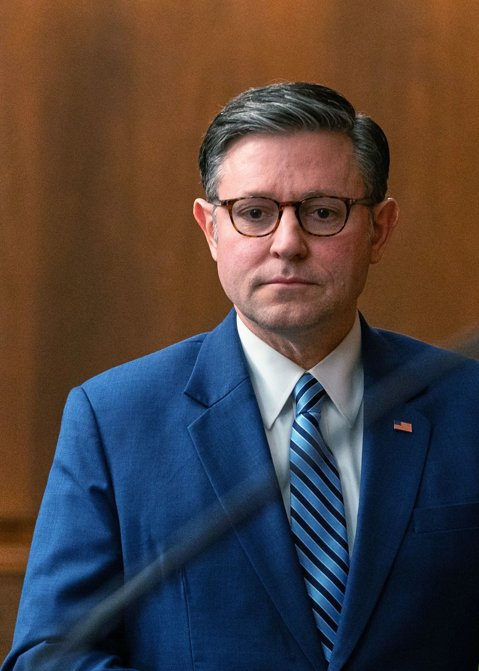 صورة لرجل يرتدي بدلة زرقاء وقميصًا أبيض مع ربطة عنق مخططة، يبدو جادًا أثناء حديثه في جلسة حكومية، تعكس التوترات السياسية حول تمويل وزارة الأمن الداخلي.