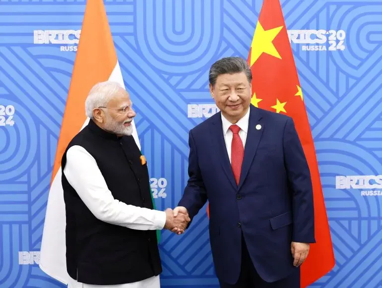 رئيس الوزراء الهندي ناريندرا مودي والرئيس الصيني شي جين بينغ يتصافحان خلال قمة BRICS 2024، مع أعلام الهند والصين خلفهما، في إطار تعزيز العلاقات الثنائية.