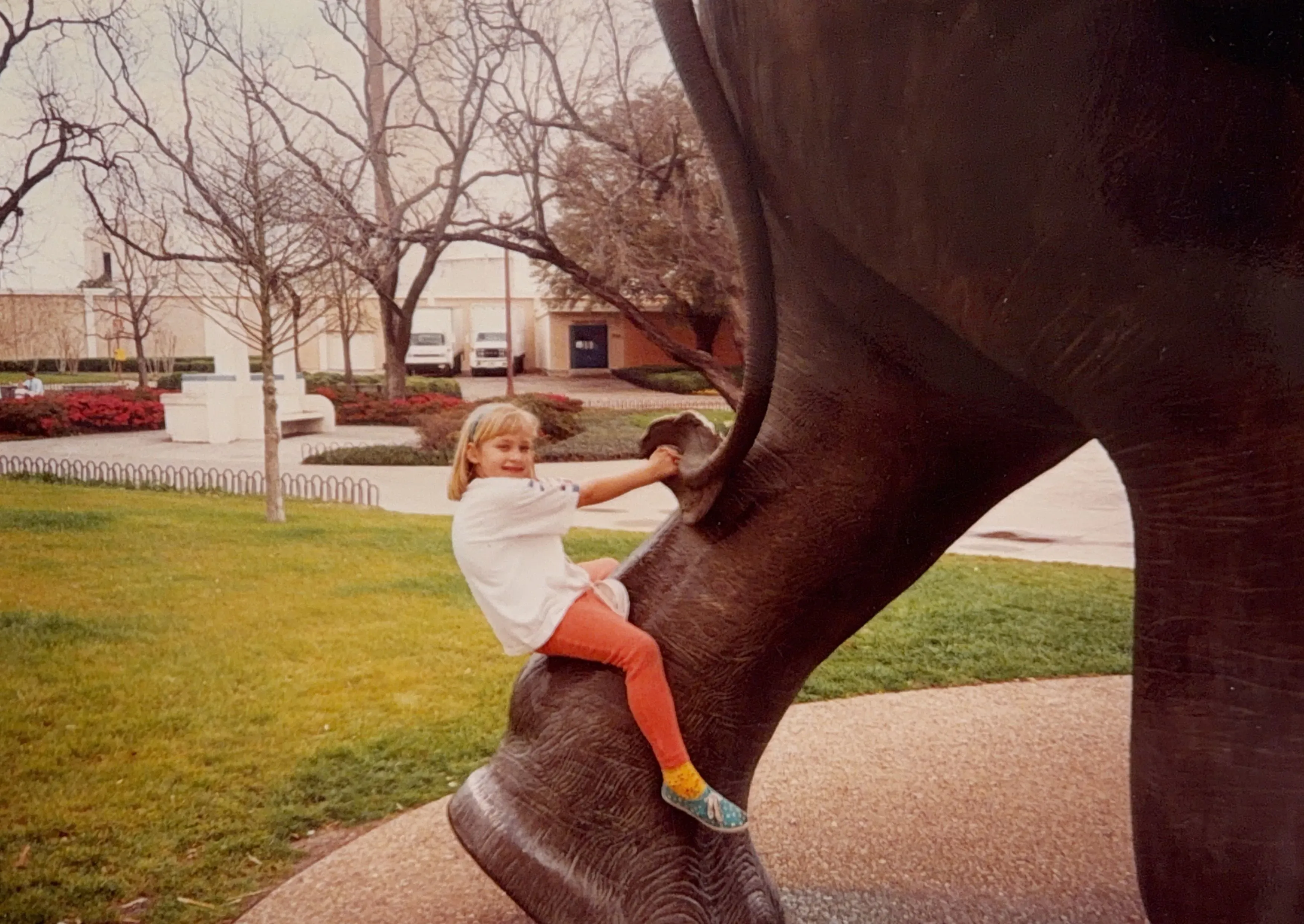 فتاة صغيرة تتسلق تمثال في حديقة، تبتسم وتلعب، مما يعكس براءة الطفولة. الصورة تتعلق بقصة كاتي وتجربتها في الحياة الأصولية.