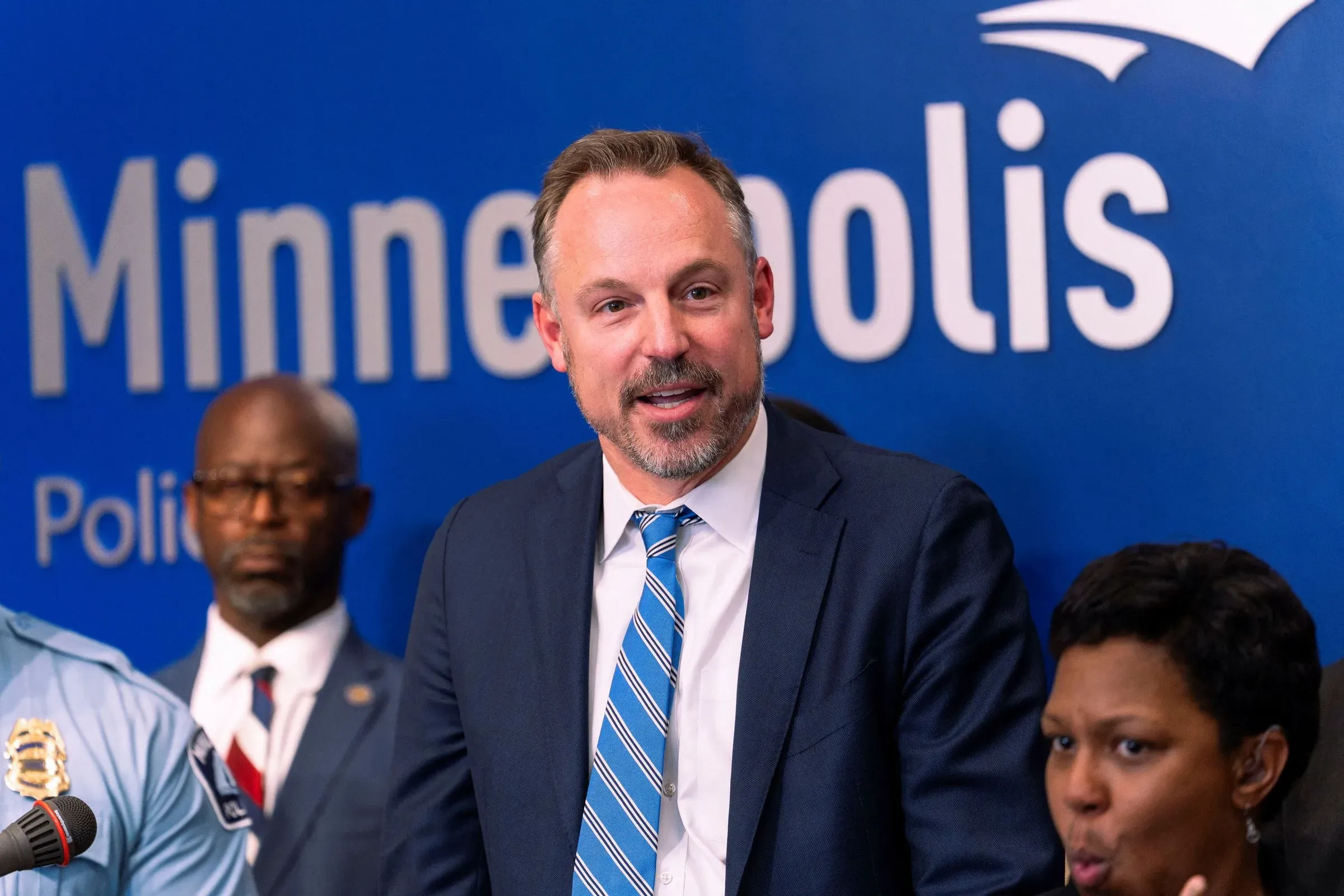 المحامي جوزيف ه. تومبسون يتحدث في مؤتمر صحفي في مينيابوليس، مع وجود ضباط شرطة خلفه، في سياق قضايا قانونية بارزة.