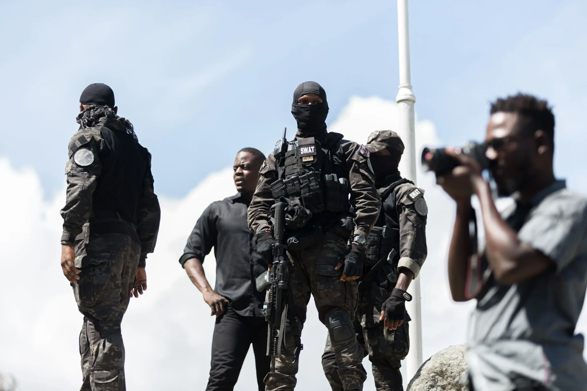عناصر من فرقة SWAT في هايتي يرتدون زيّاً عسكرياً ويحملون أسلحة، مع مصوّر فوتوغرافي يوثق المشهد، في سياق تصاعد العنف باستخدام الطائرات المسيّرة في أمريكا اللاتينية.