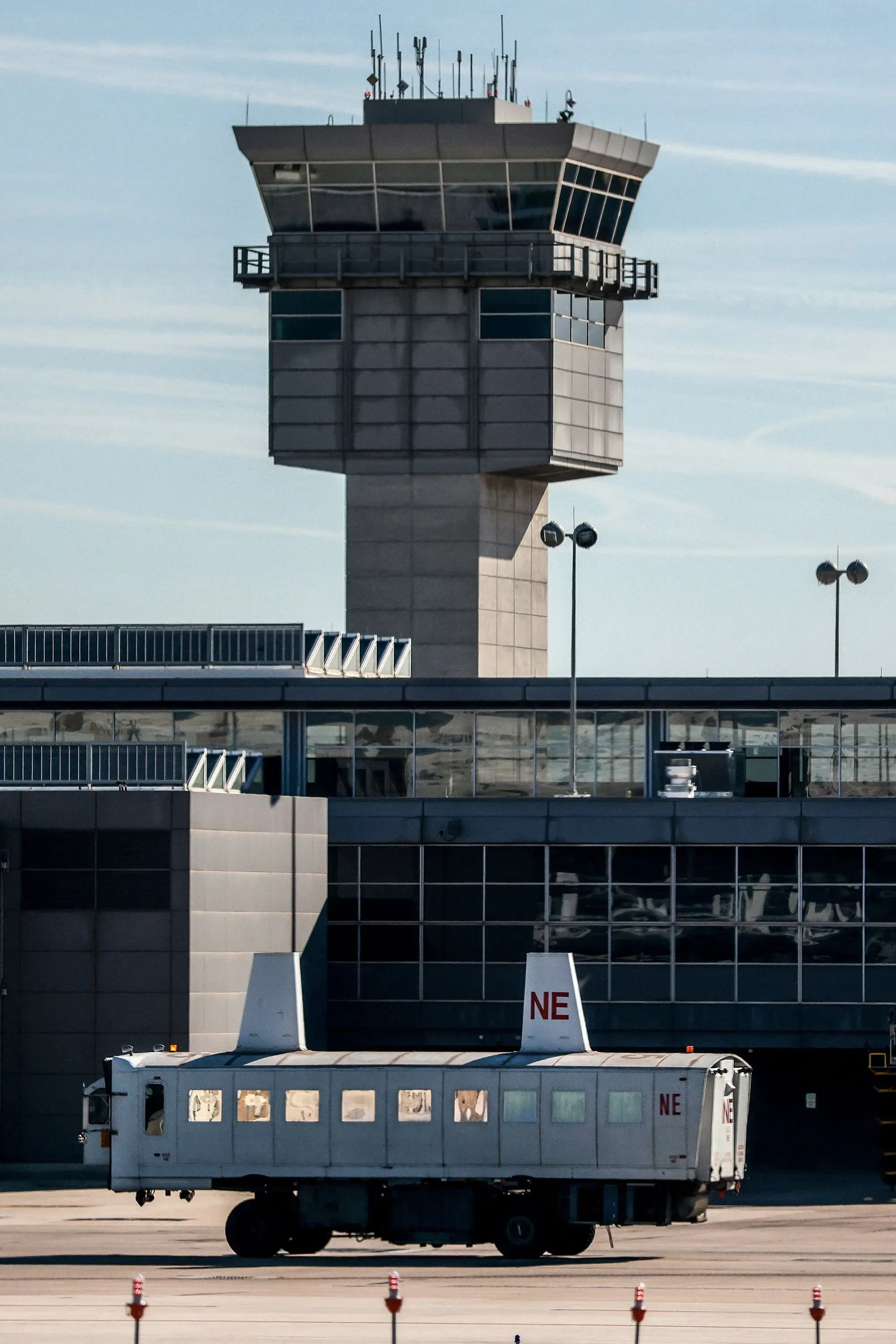 مركبة نقل الركاب المتنقلة في مطار دالاس الدولي، مع برج المراقبة في الخلفية، تُظهر التحديات التي يواجهها المطار.