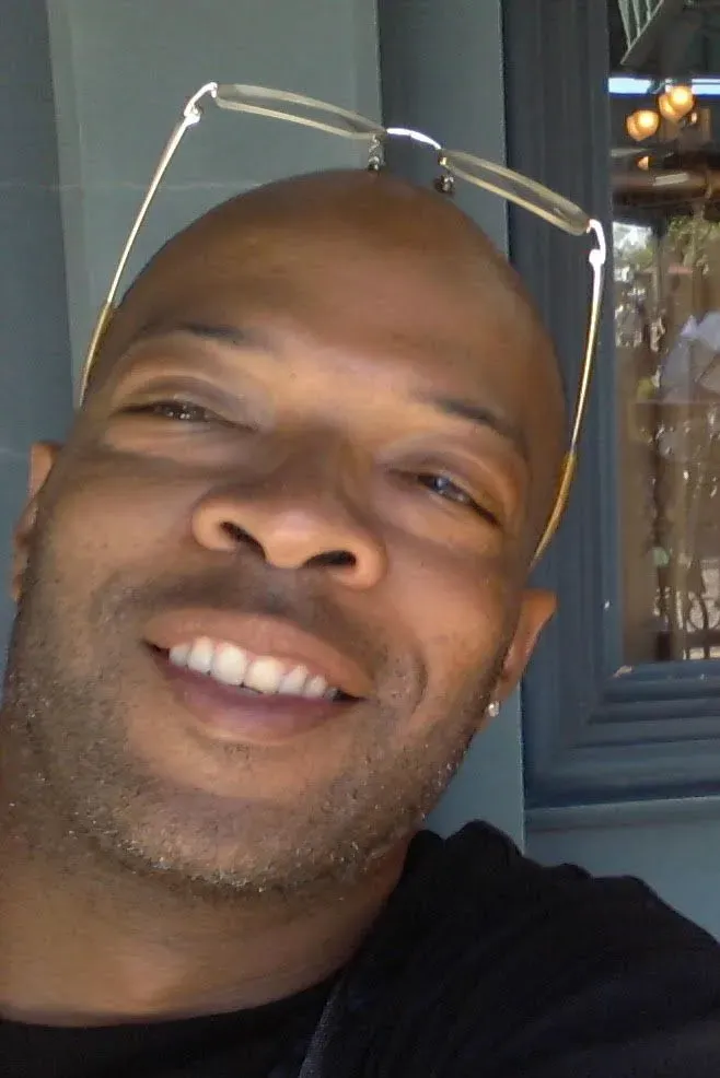 صورة لرجل مبتسم يرتدي نظارات، يظهر في مكان داخلي مشمس. تعكس الصورة روح الأمل والتواصل الإنساني في ظل قضايا الاحتجاز.