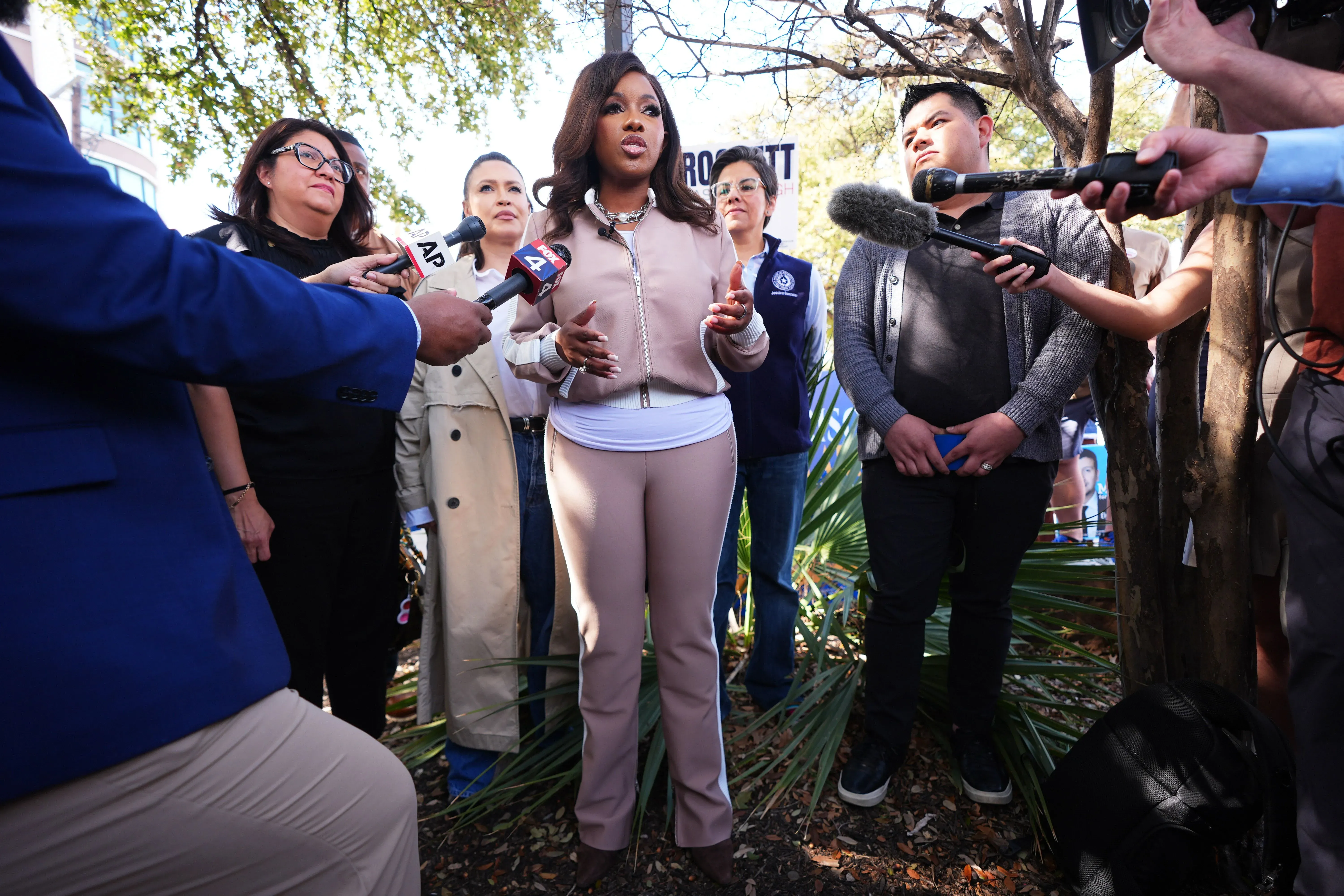 امرأة تتحدث إلى مجموعة من الصحفيين أثناء حدث انتخابي في تكساس، مع وجود أشخاص آخرين في الخلفية، مما يعكس النشاط السياسي في الانتخابات التمهيدية.