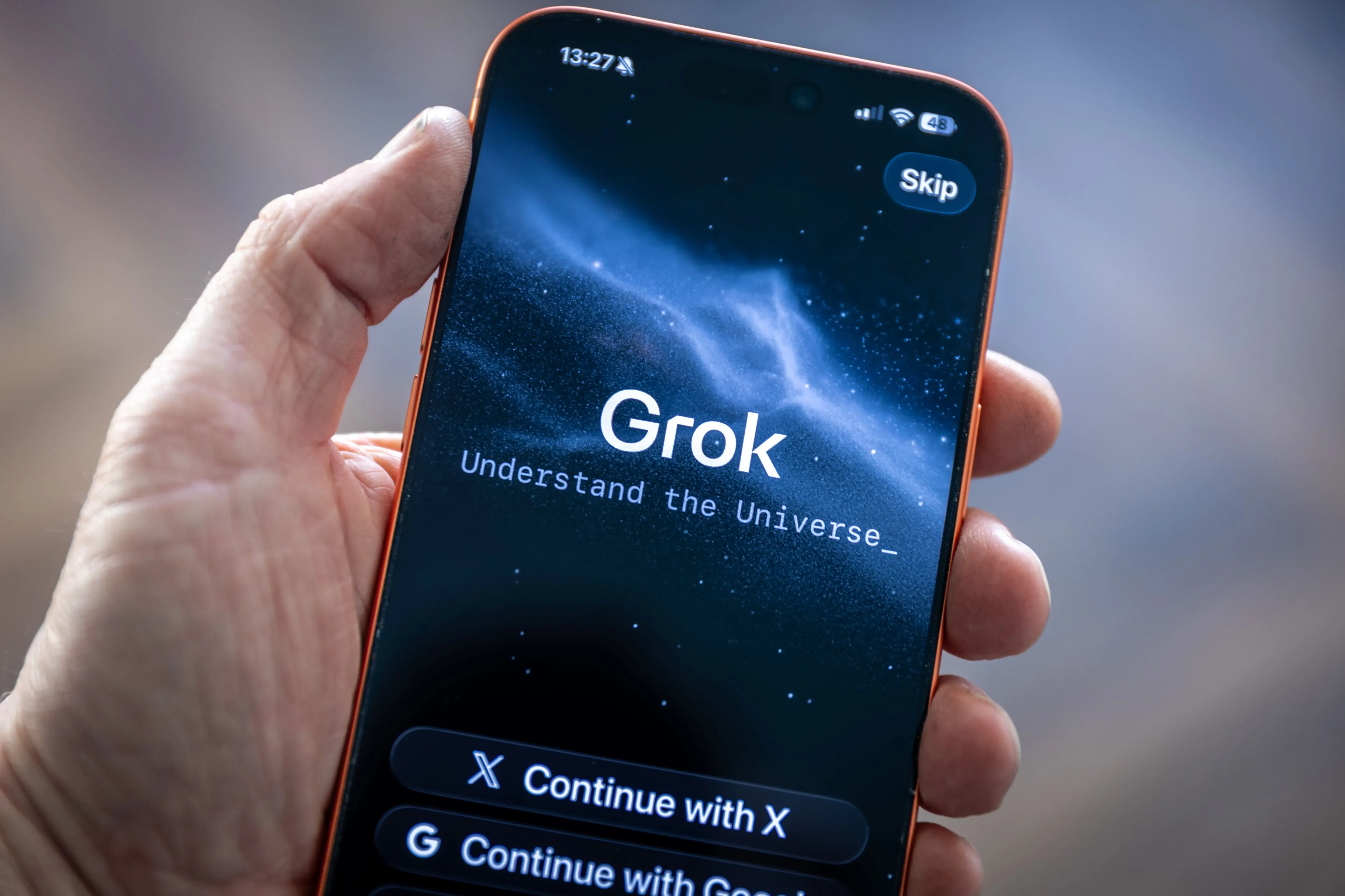شاشة هاتف ذكي تعرض واجهة تطبيق "Grok" مع عبارة "افهم الكون"، مما يسلط الضوء على استخدام الذكاء الاصطناعي في التواصل الاجتماعي.