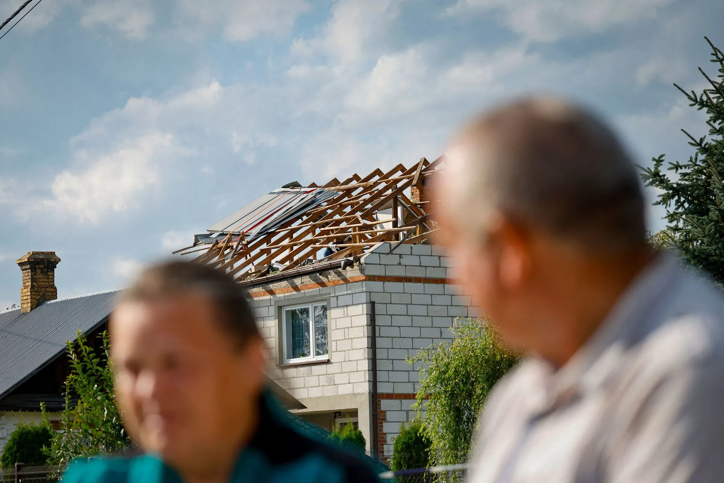 تظهر الصورة منزلًا تضرر سقفه، مع شخصين يجلسان في المقدمة. تعكس الأضرار التوترات الأمنية المتزايدة في أوروبا.