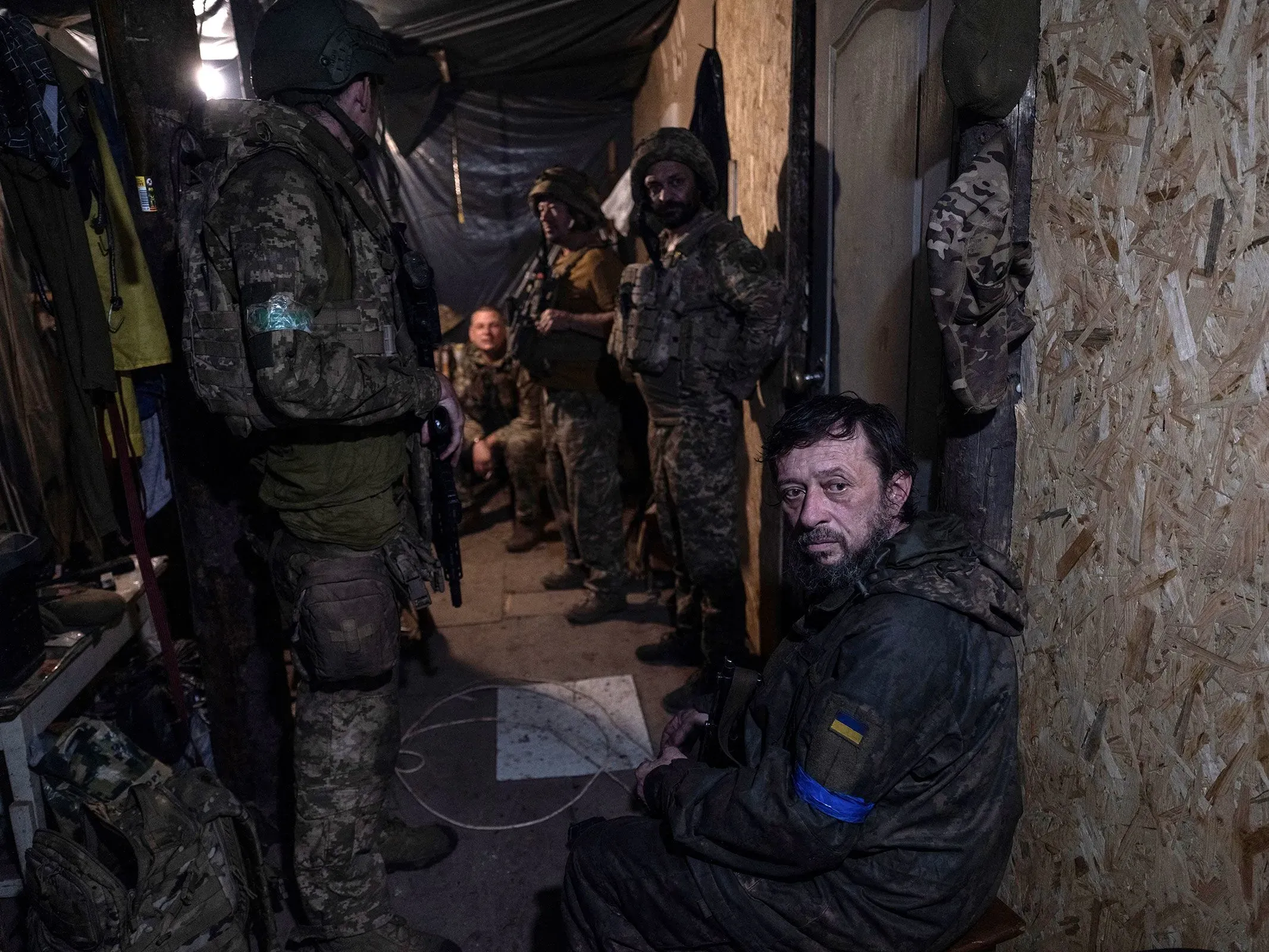 جنود أوكرانيون في ملجأ تحت الأرض، يتبادلون الحديث بجدية، مع وجود معدات عسكرية حولهم، تعكس أجواء الحرب والتوتر في المنطقة.