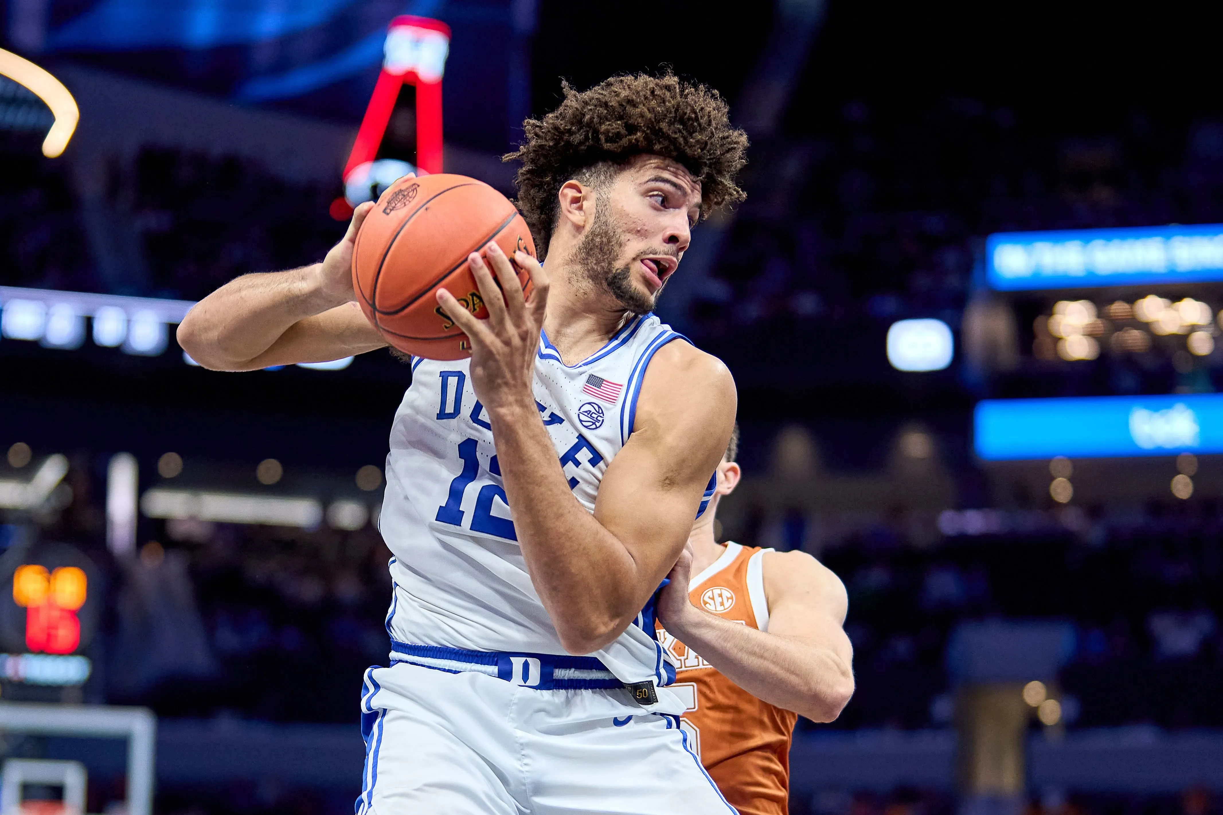 لاعب كرة سلة من فريق ديوك، يحمل الكرة ويستعد للتمرير، مع وجود لاعب آخر بالقرب منه في سياق مباراة NCAA.