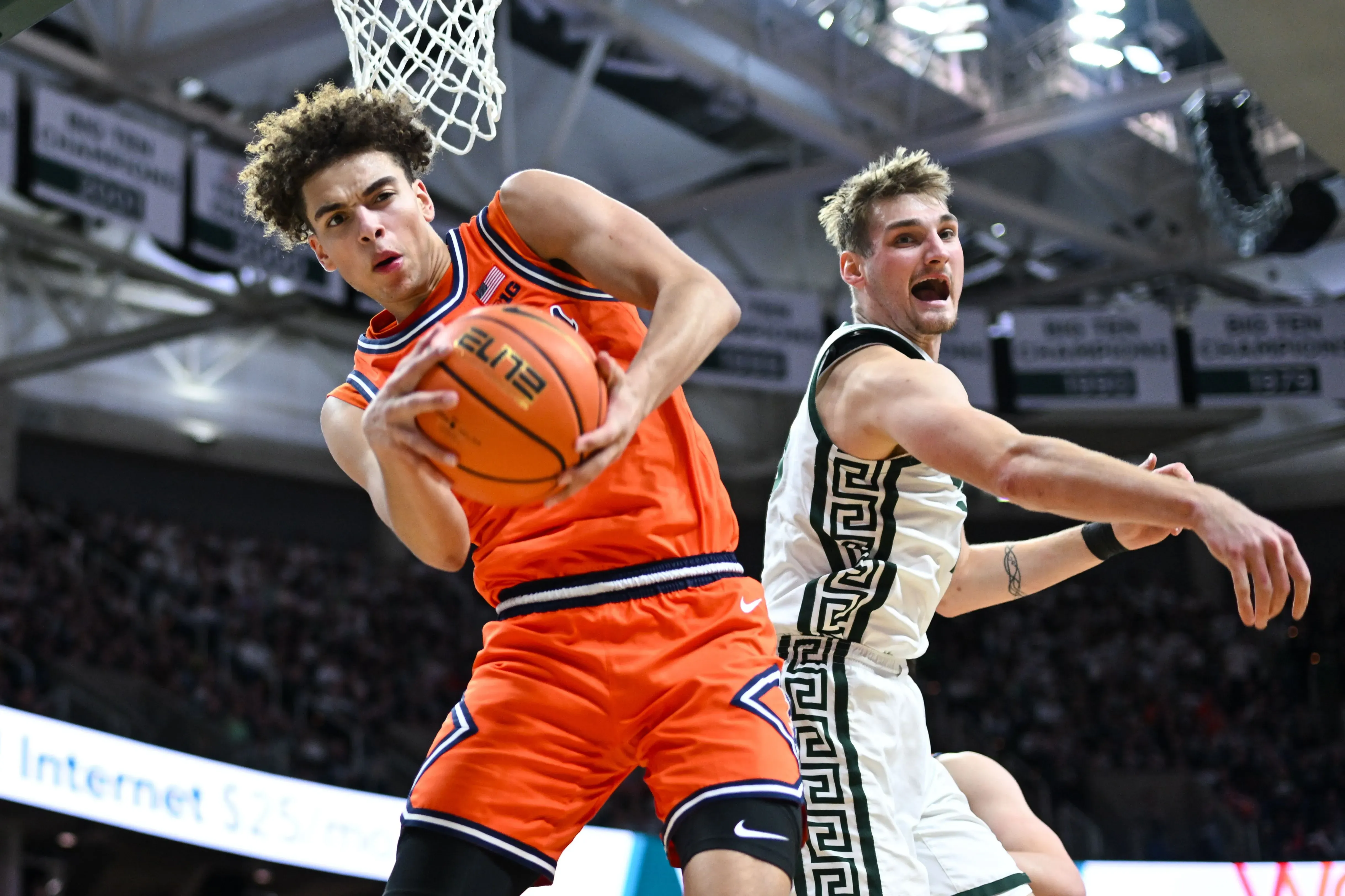 لاعب كرة سلة يرتدي زيًا برتقاليًا، يستعد للتمريرة بينما يواجه لاعبًا آخر في ملعب مزدحم، مما يعكس أجواء المنافسة في بطولة NCAA.