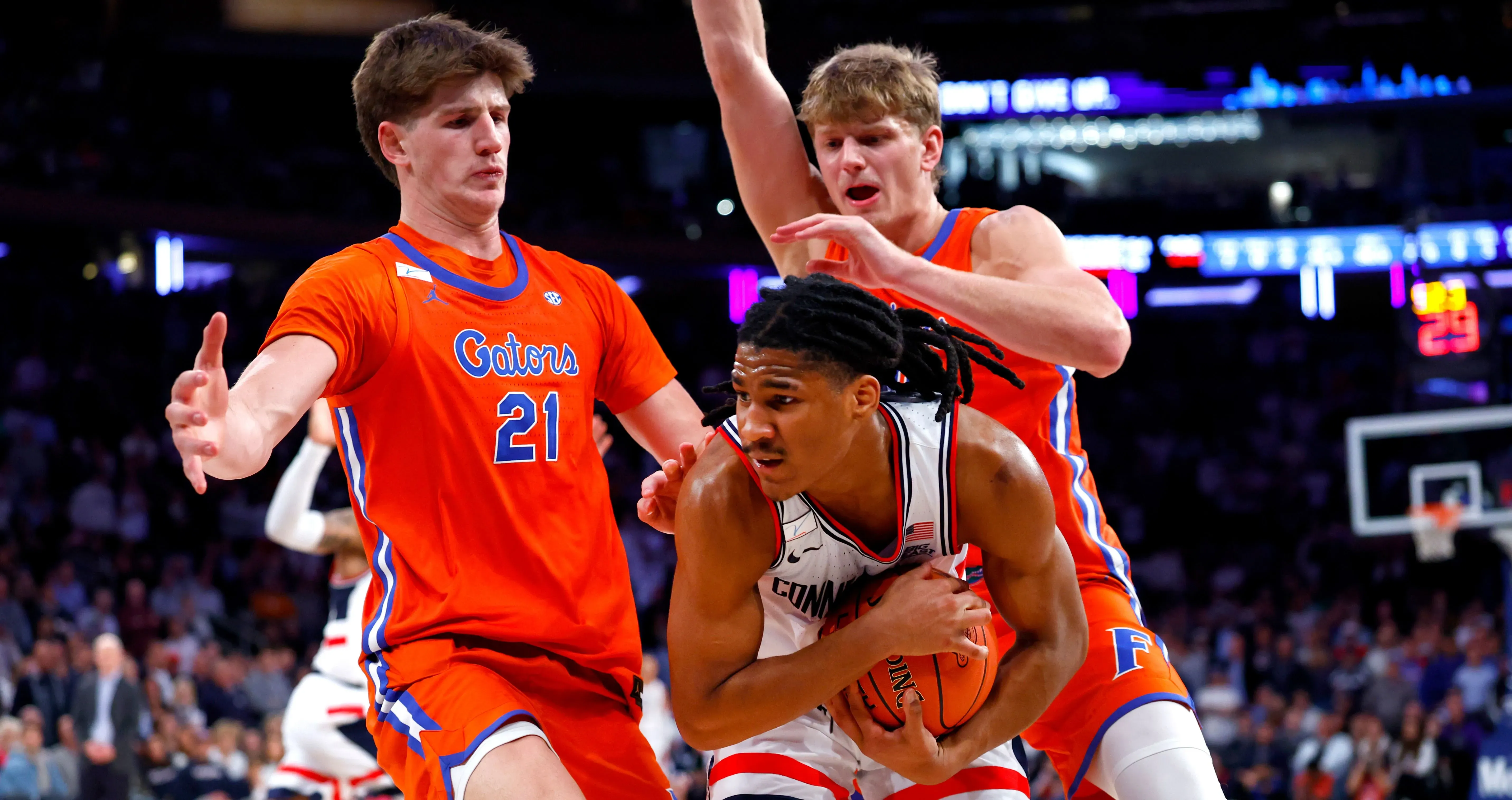 لاعب كرة سلة من فريق جامعة كونكتيكت يتعرض للضغط من لاعبين من فريق فلوريدا خلال مباراة NCAA، مع التركيز على التنافس الشديد.