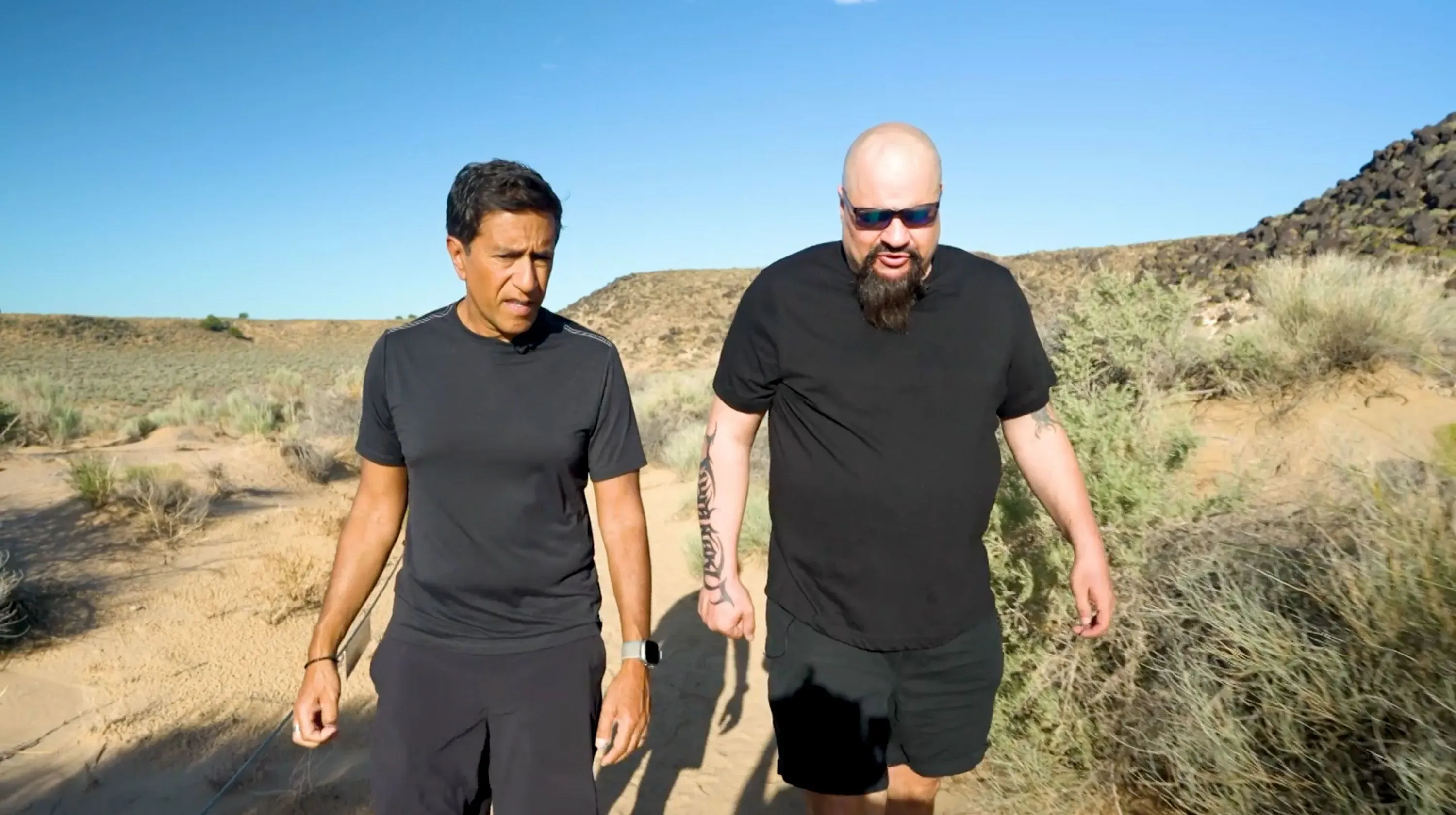 د. سانجاي غوبتا وإدوارد موري يسيران في منطقة صحراوية، يتحدثان عن تجارب الألم المزمن وأساليب العلاج الحديثة.