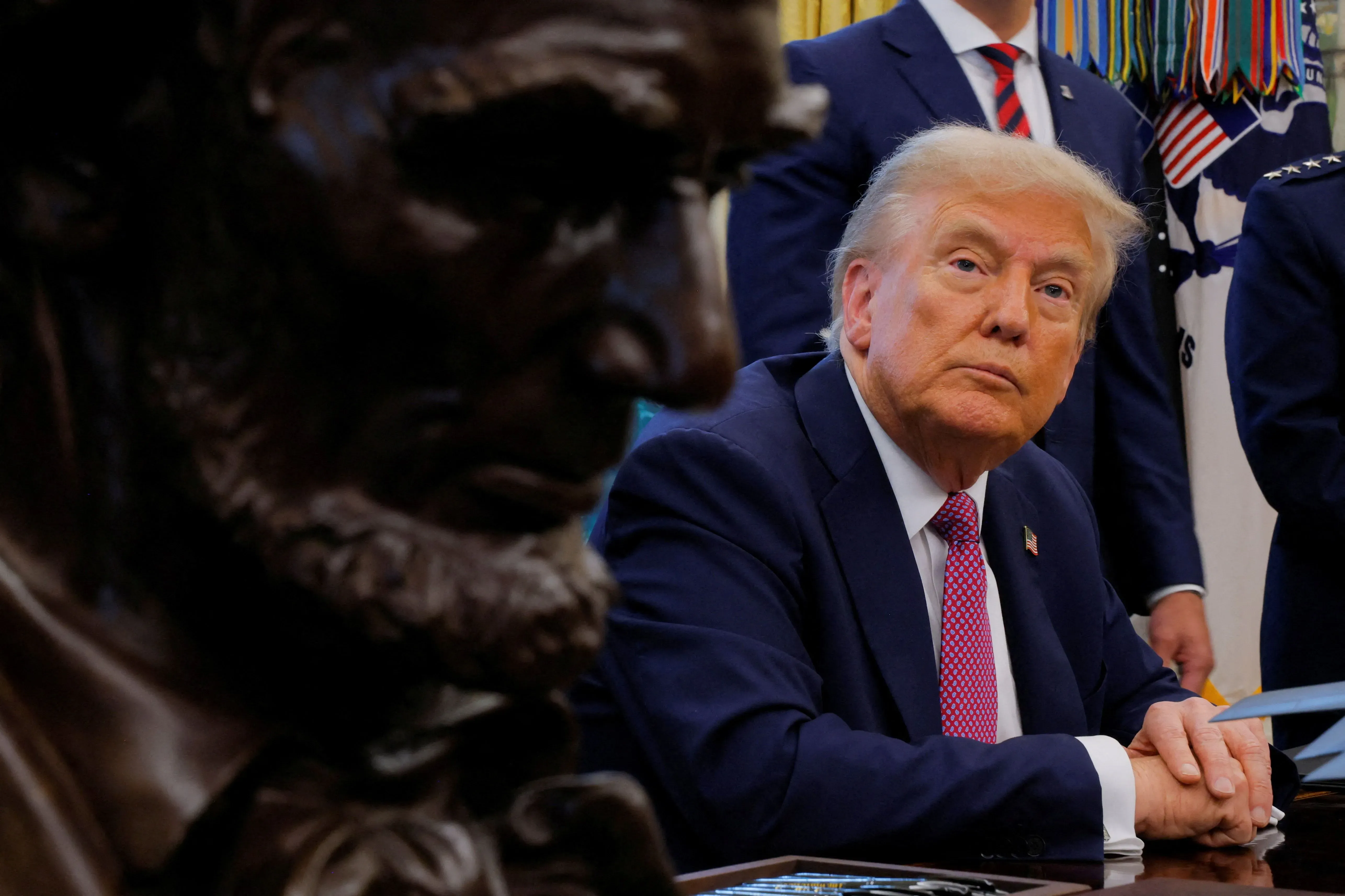 صورة لدونالد ترامب في المكتب البيضاوي، ينظر بجدية نحو تمثال لأبراهام لنكولن، مع وجود موظفين خلفه. تعكس الصورة التوترات القانونية حول الضربة العسكرية الأخيرة.