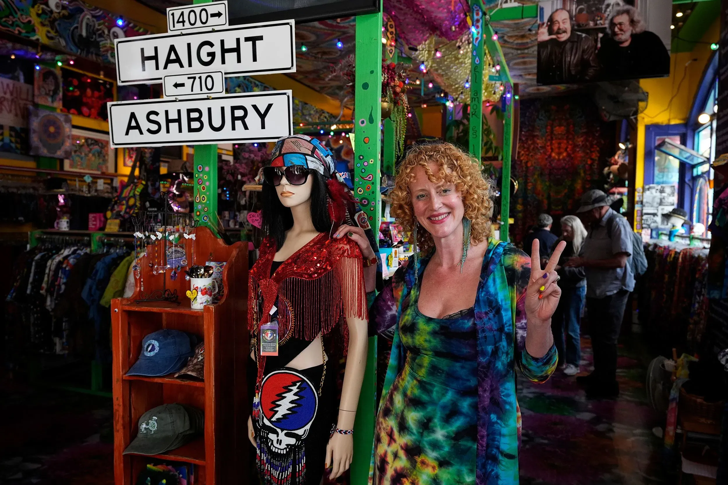امرأة مبتسمة ترتدي ملابس ملونة تقف بجانب دمية في متجر في حي هايت-أشبوري، حيث يحتفل معجبو فرقة Grateful Dead بثقافة الهيبي.