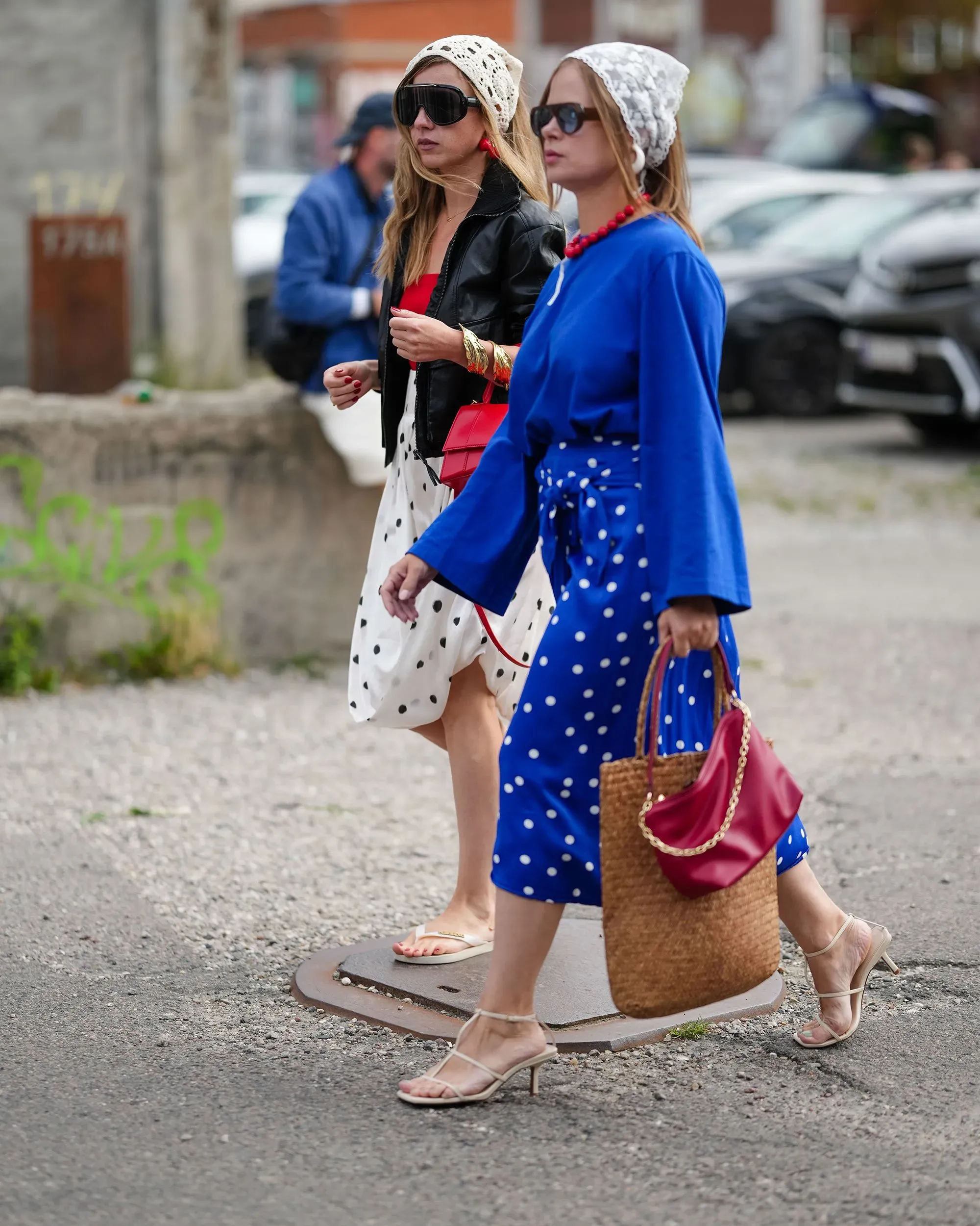 امرأتان تسيران في الشارع، إحداهما ترتدي فستاناً أبيض مزخرفاً بالنقاط السوداء والأخرى بفستان أزرق مزخرف بالنقاط، مع أكسسوارات عصرية.