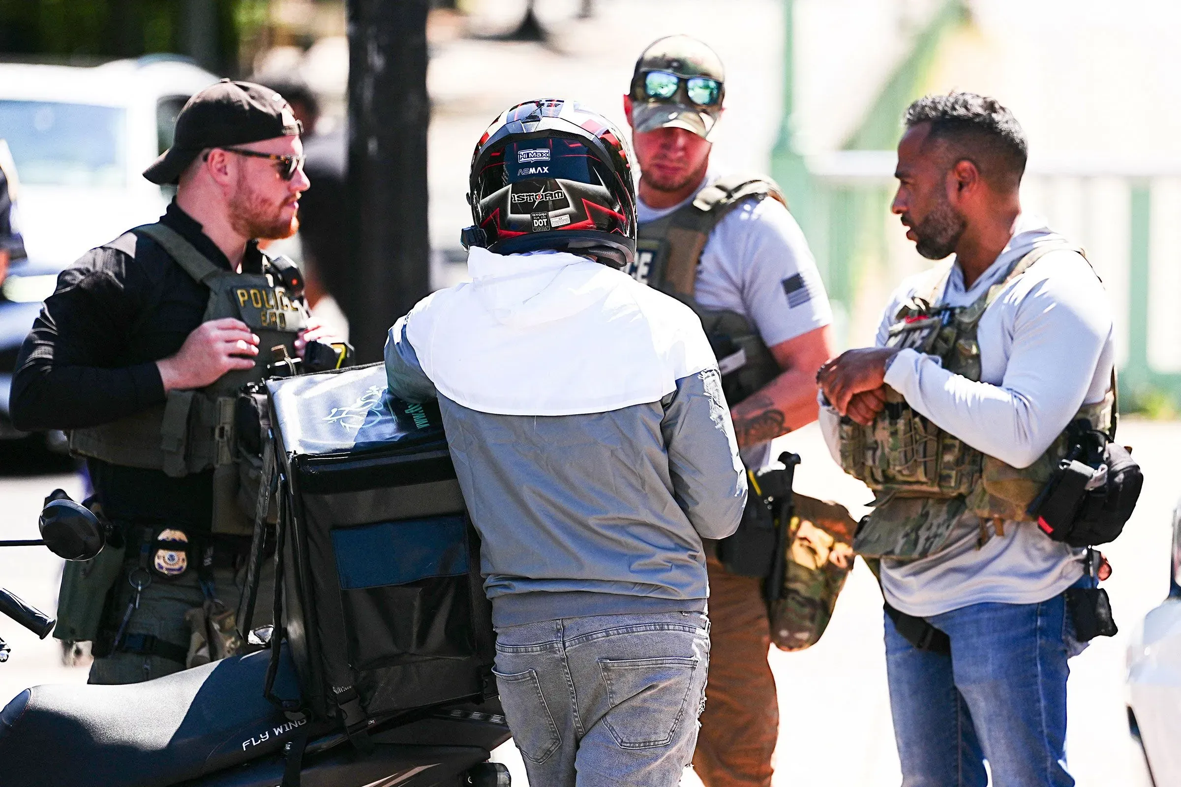 سائق توصيل يرتدي خوذة ويتحدث مع ضباط إنفاذ القانون في واشنطن، مع توتر واضح بسبب زيادة الاعتقالات المتعلقة بالمهاجرين.