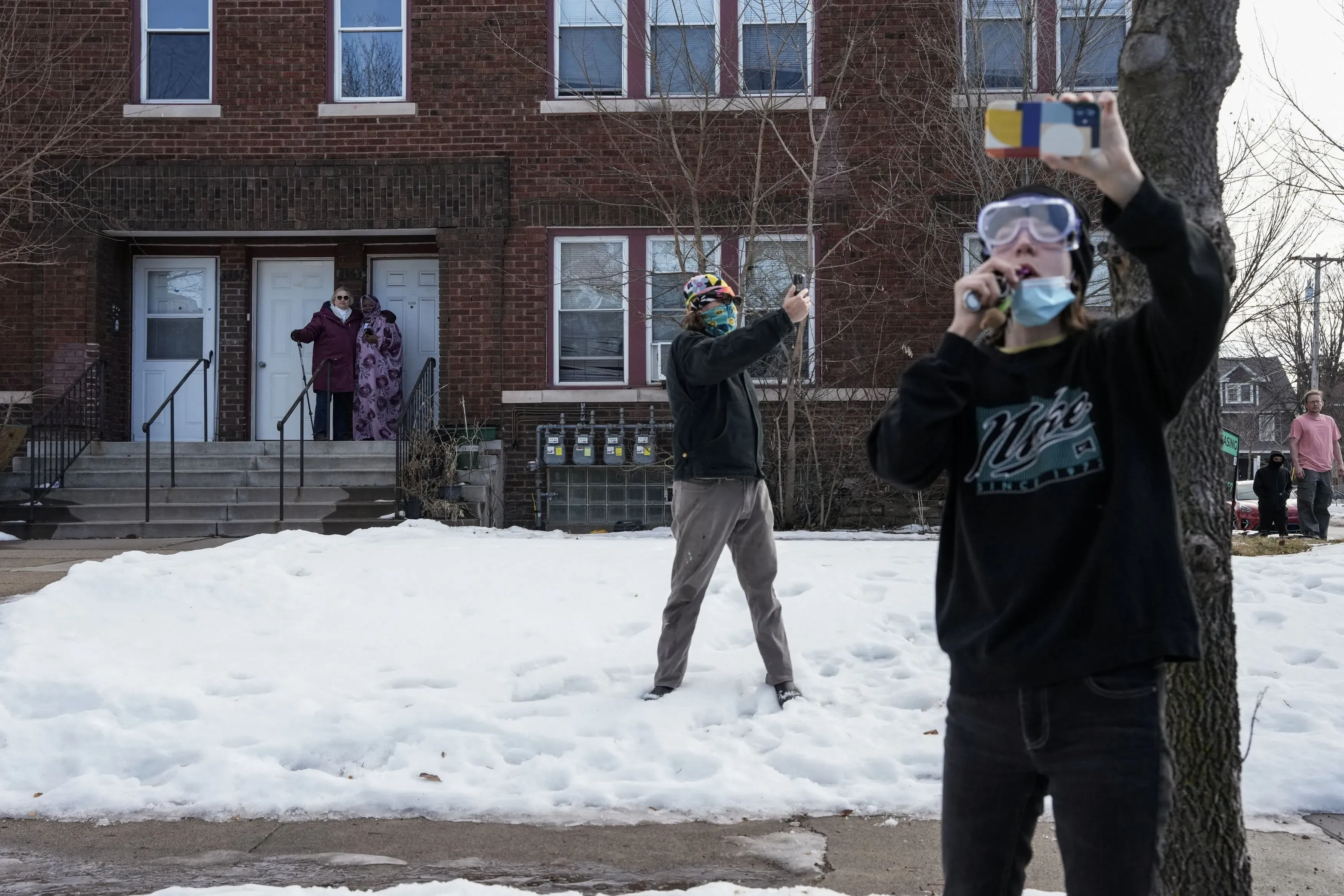 مجموعة من المتطوعين يرتدون أقنعة واقية، يقومون بتوثيق نشاطات عملاء الهجرة في مينيسوتا، وسط الثلوج، في سياق زيادة المراقبة بعد حادث إطلاق النار.