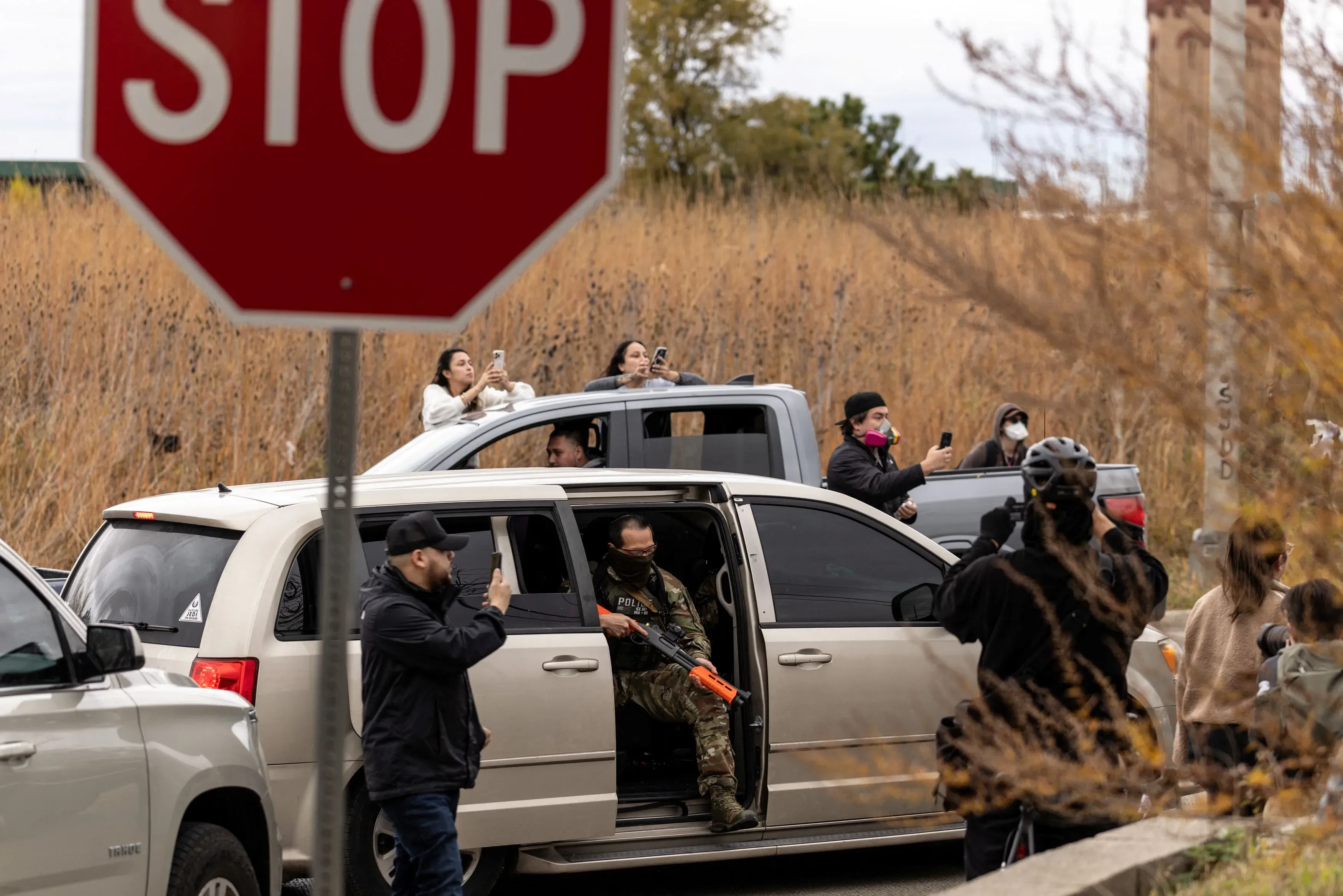 مجموعة من المتطوعين تراقب عملاء الهجرة في مينيابوليس، مع وجود لافتة توقف في الخلفية، تعكس نشاطات المراقبة القانونية بعد حادثة مميتة.