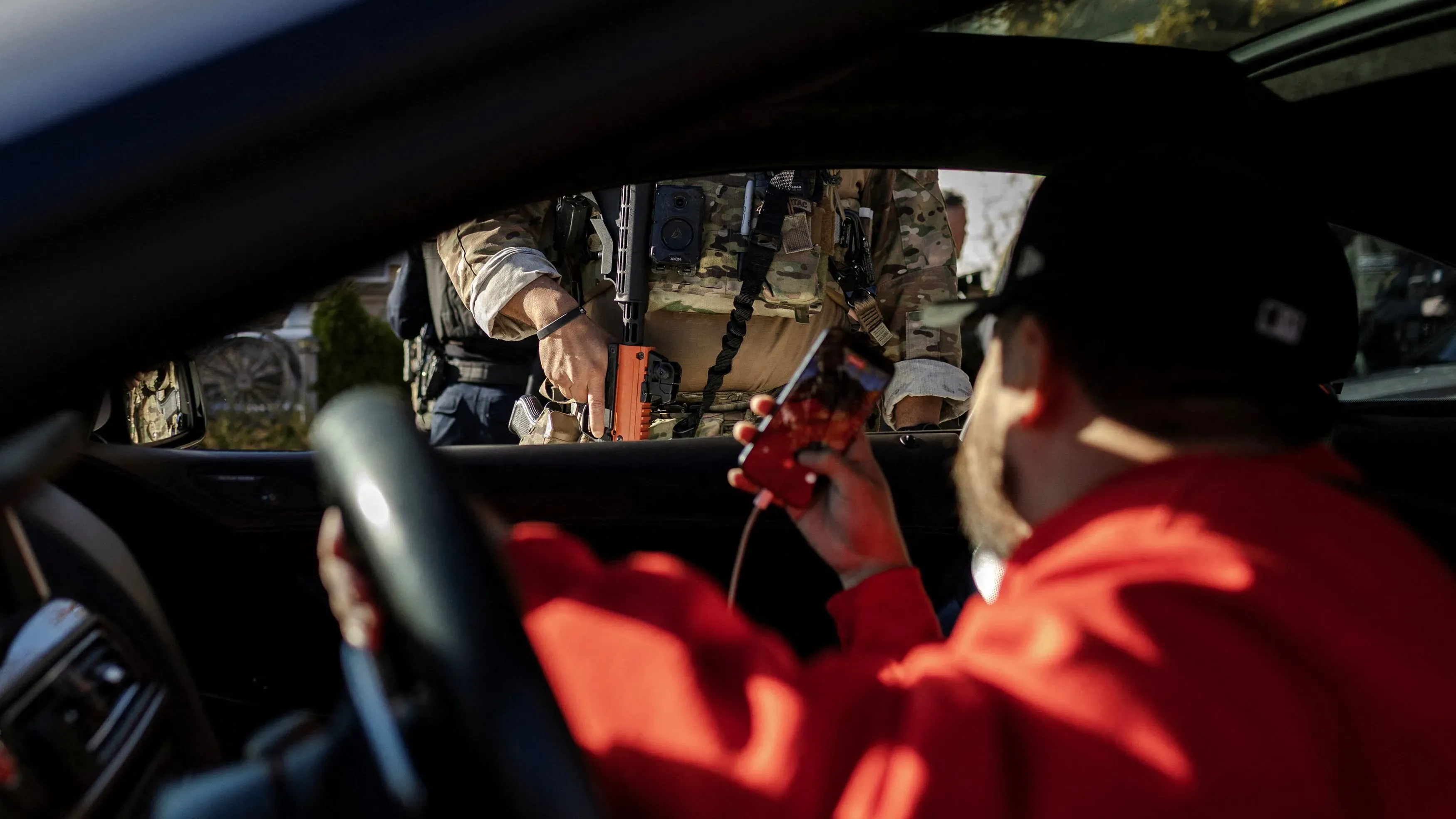 رجل يجلس في سيارة ويصور ضابطًا من إدارة الهجرة والجمارك أثناء عملية اعتقال، مما يعكس جهود المراقبة القانونية في مينيسوتا.