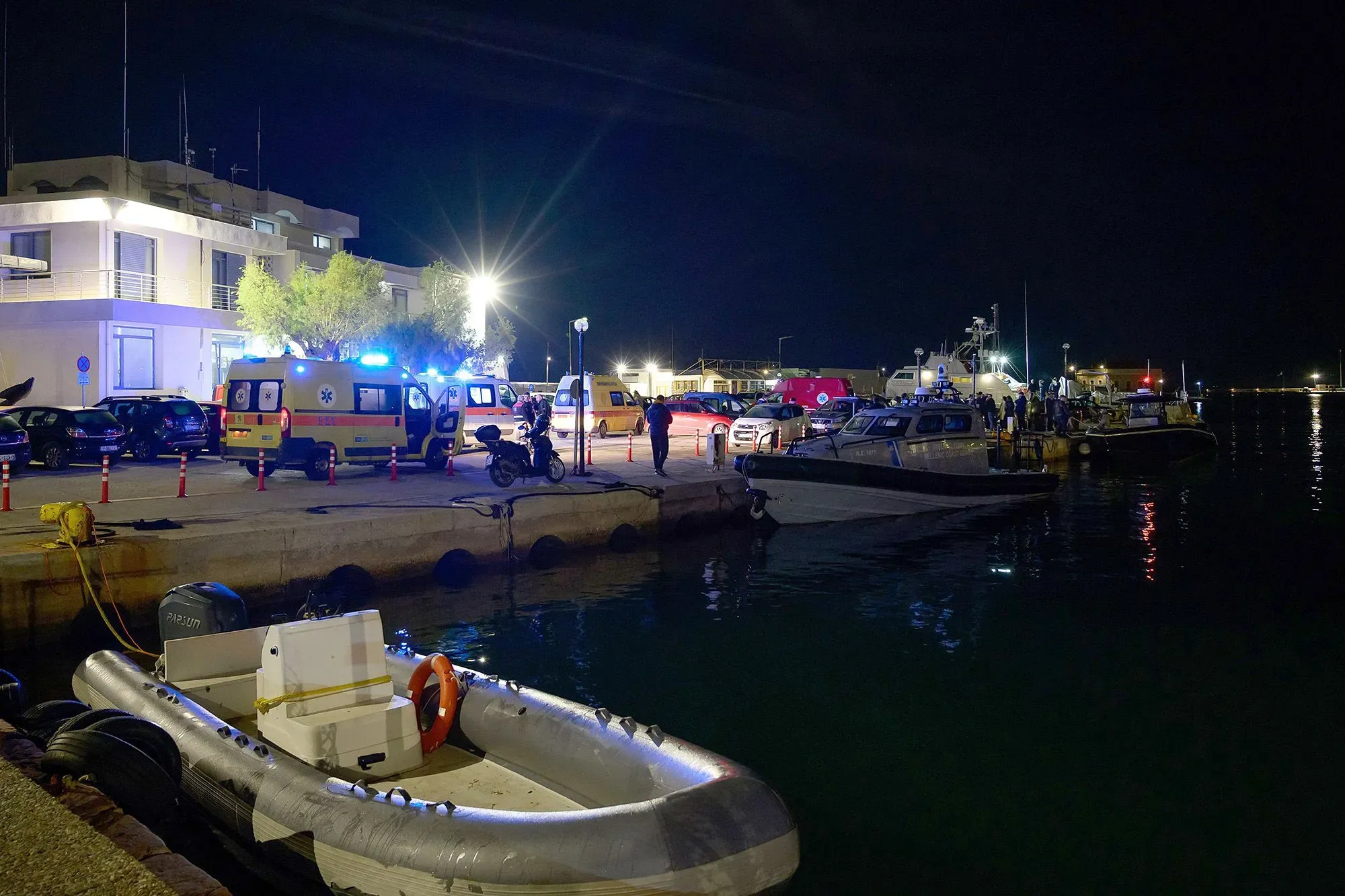 نشاطات إنقاذ في ميناء خيوس بعد غرق قارب مهاجرين، مع وجود سيارات إسعاف وسفن خفر السواحل في موقع الحادث.