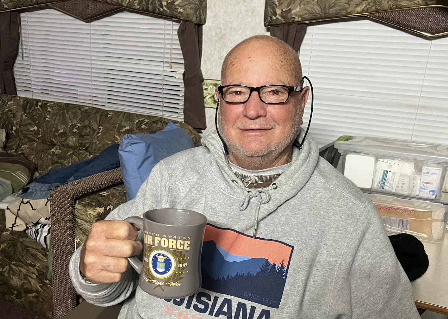 رجل مسن يجلس في غرفة معيشة، يحمل كوبًا مكتوبًا عليه "سلاح الجو الأمريكي"، ويبدو في حالة جيدة بعد تعافيه من عدوى خطيرة.