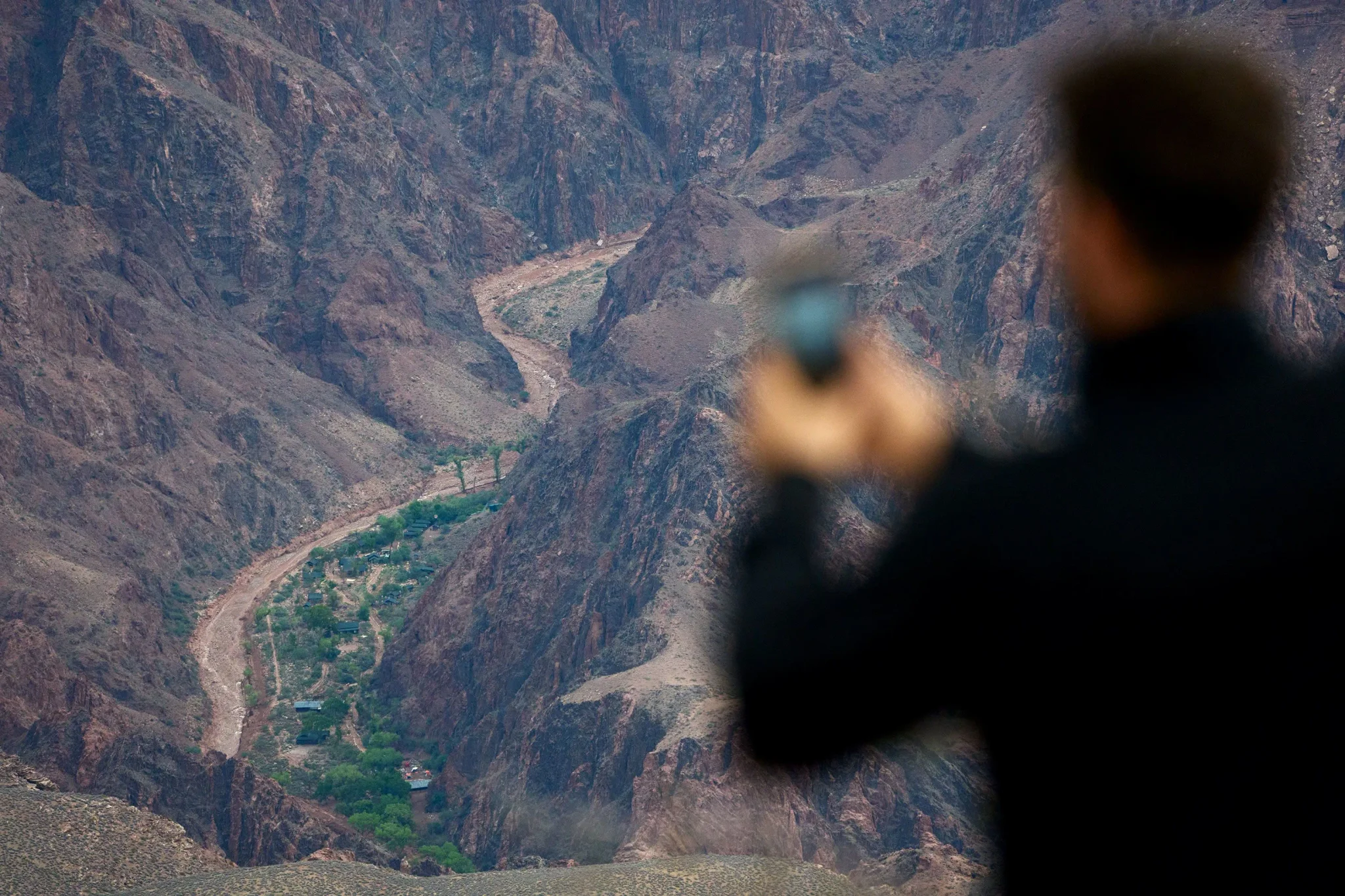 رجل يلتقط صورة لمحطة Phantom Ranch التاريخية في قاع وادي Grand Canyon وسط الجبال الصخرية، مع نهر Bright Angel Creek.