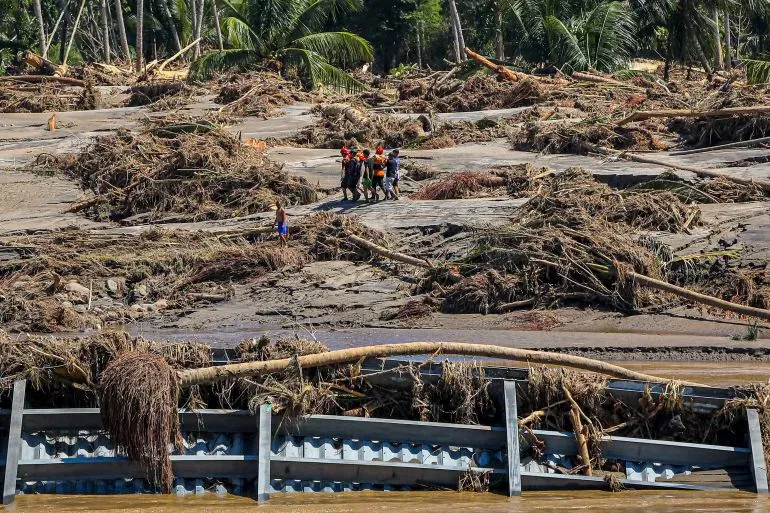 أفراد من فرق الإنقاذ يسيرون عبر منطقة متضررة من الفيضانات والانهيارات الأرضية، حيث تغطي الحطام والطين الأرض.