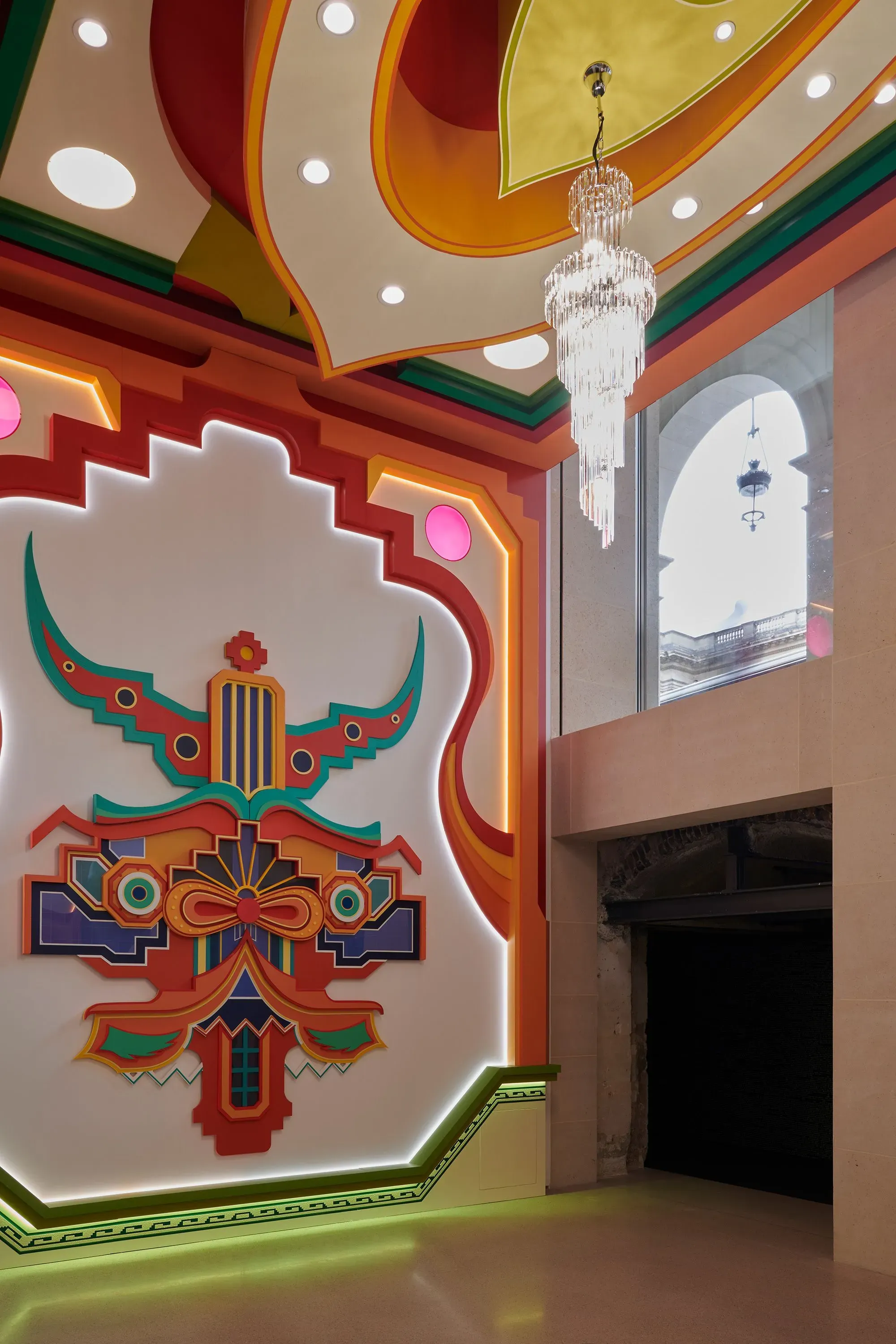 تصميم داخلي لمتحف كارتييه الجديد في باريس، يظهر جدارًا مزخرفًا بألوان زاهية وثريا معاصرة، مع نوافذ كبيرة تسمح بدخول الضوء الطبيعي.