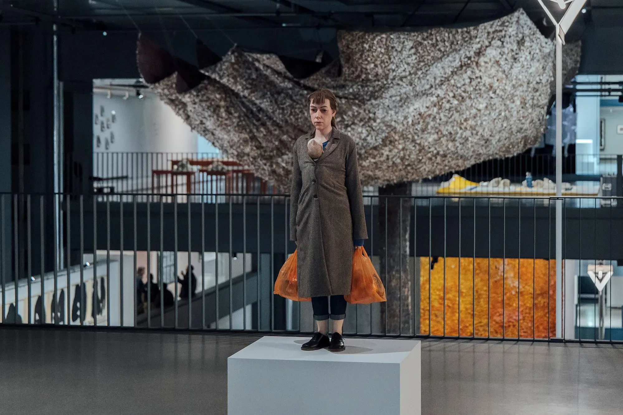 امرأة واقفة على قاعدة عرض في متحف كارتييه، تحمل أكياساً برتقالية، محاطة بأعمال فنية معاصرة ومساحات عرض مفتوحة.