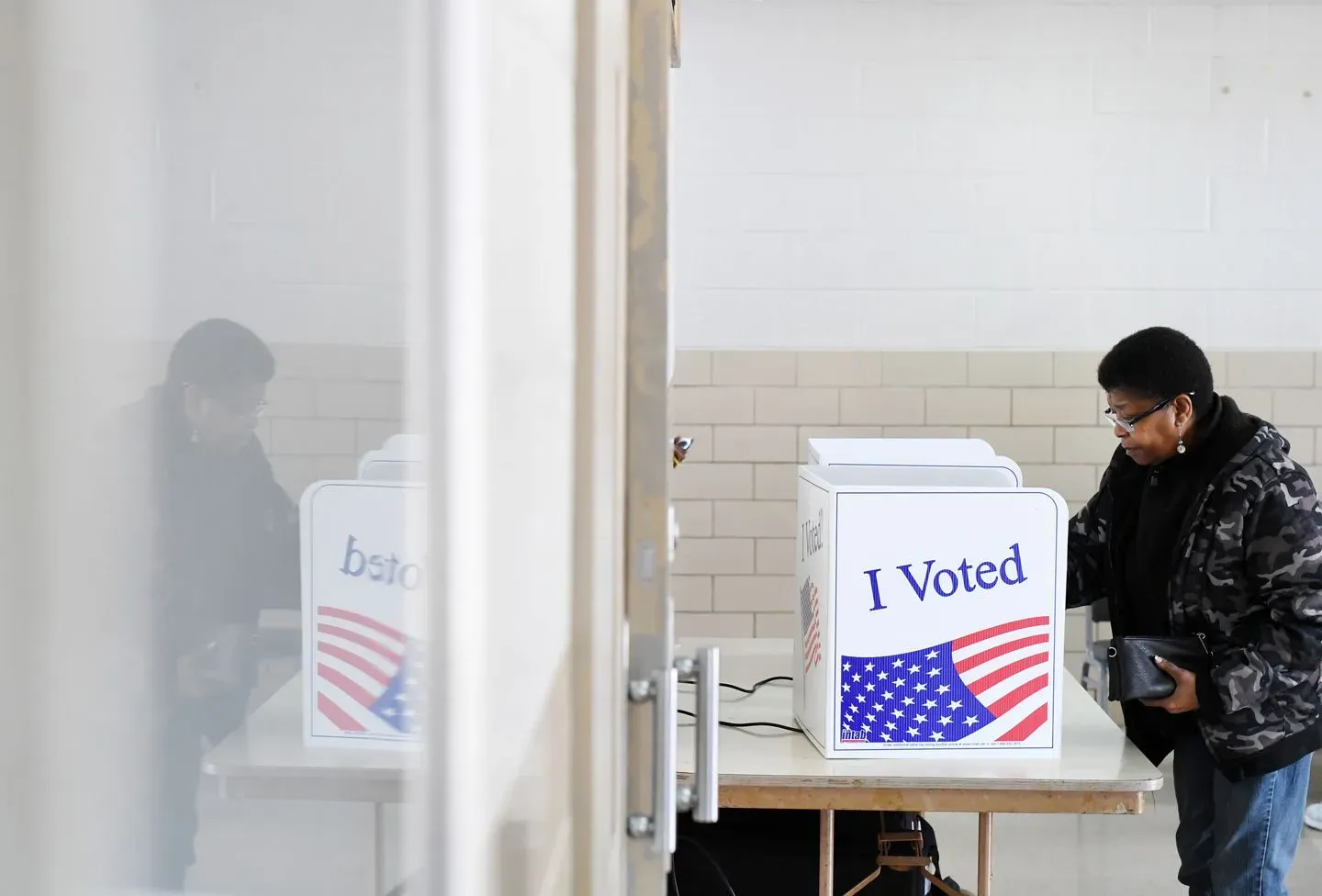 امرأة تصوت في مركز اقتراع، مع صندوق اقتراع يحمل عبارة "لقد صوتت" وخلفية بسيطة، تعكس أهمية المشاركة الديمقراطية في الانتخابات.