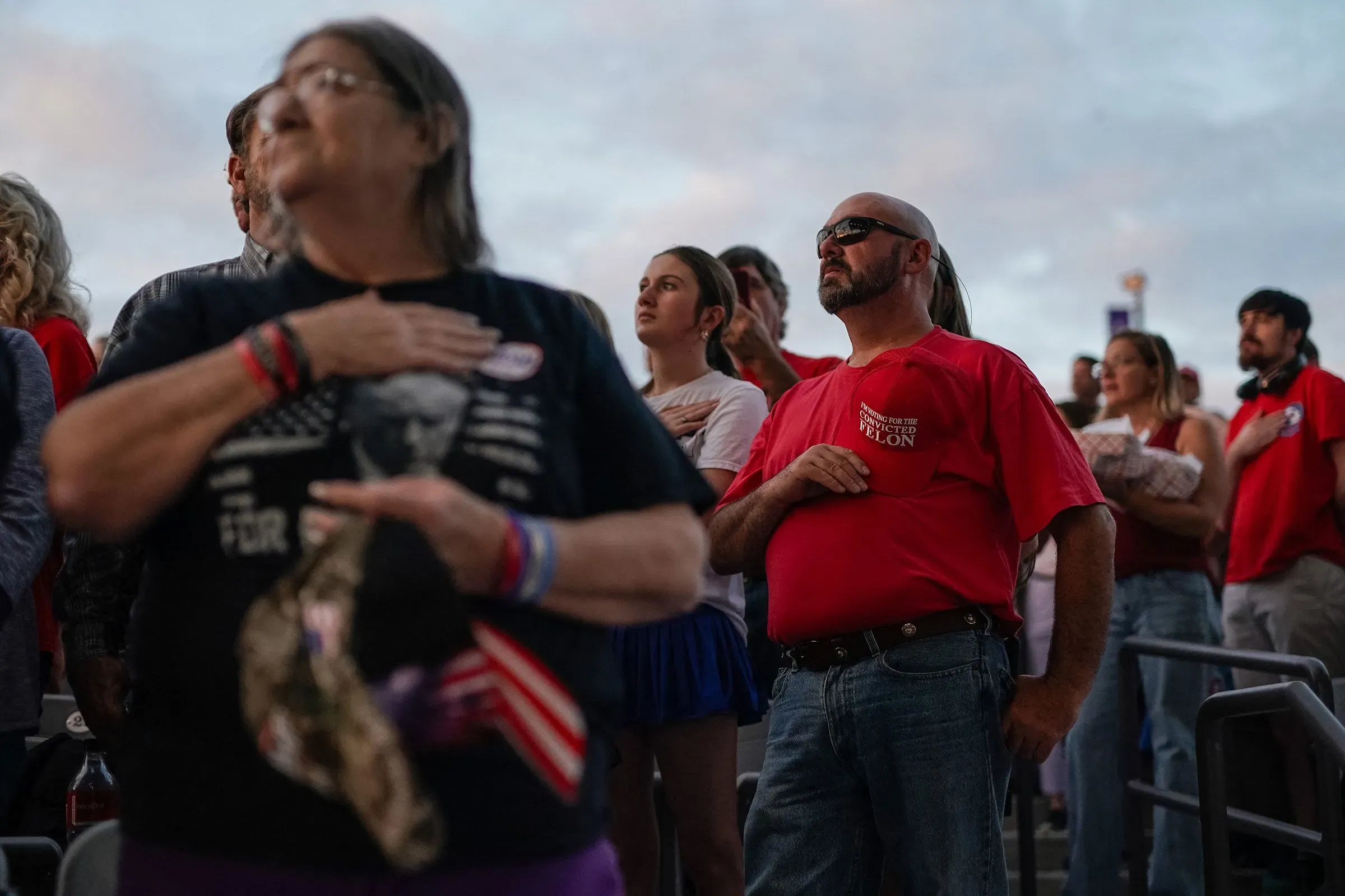 حشد من الناخبين يرتدون قمصانًا تحمل شعارات سياسية، يرفعون أيديهم في إشارة الولاء خلال حدث انتخابي لدعم ترامب.