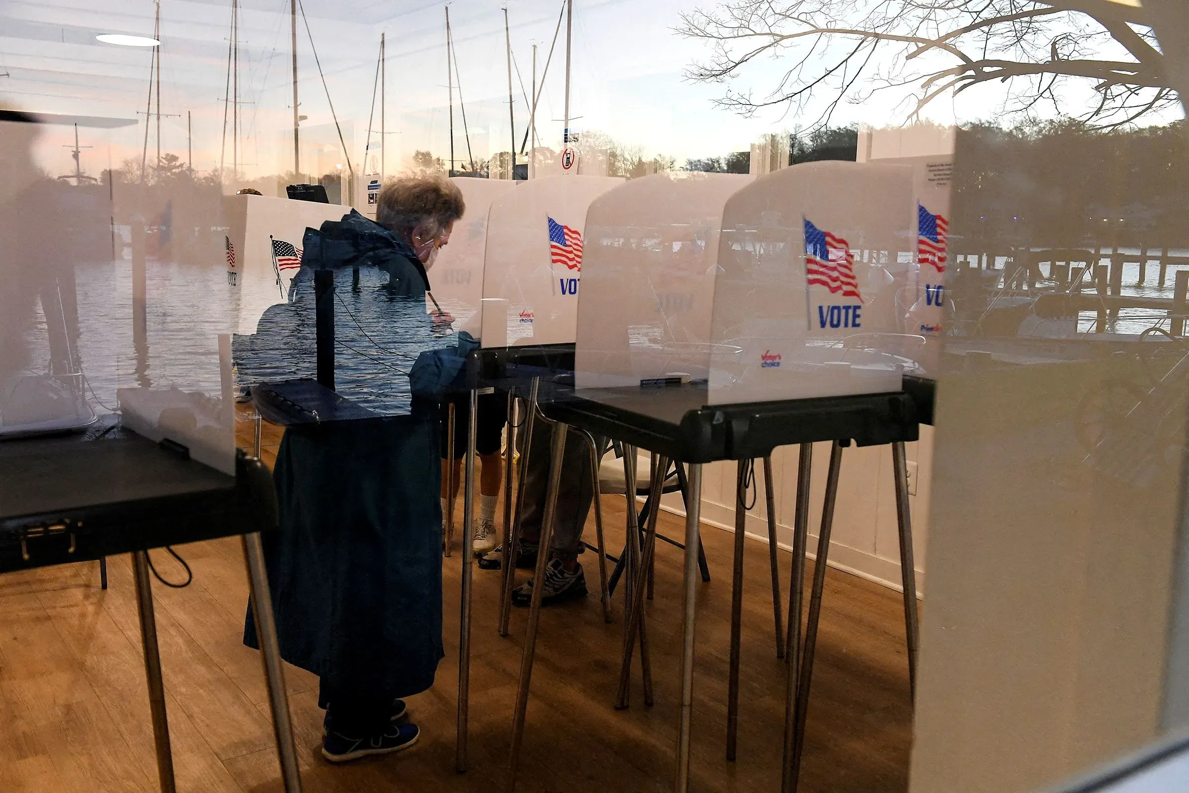 ناخبون في مركز اقتراع، يظهرون خلف حواجز التصويت، مع لافتات "صوت" وأعلام أمريكية، مما يعكس أهمية الانتخابات في 2024.