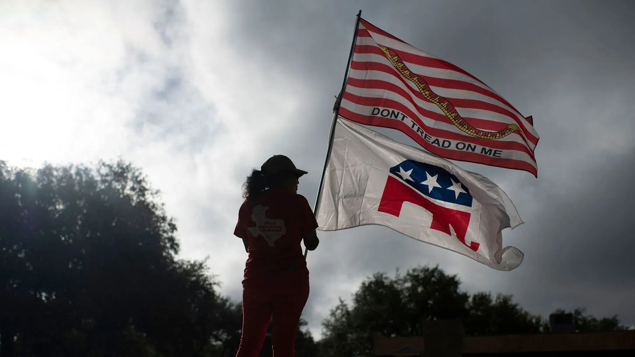 امرأة تحمل علمين، أحدهما يحمل شعار "لا تلمسني" والآخر شعار الحزب الجمهوري، في أجواء غائمة تعكس التوترات السياسية.