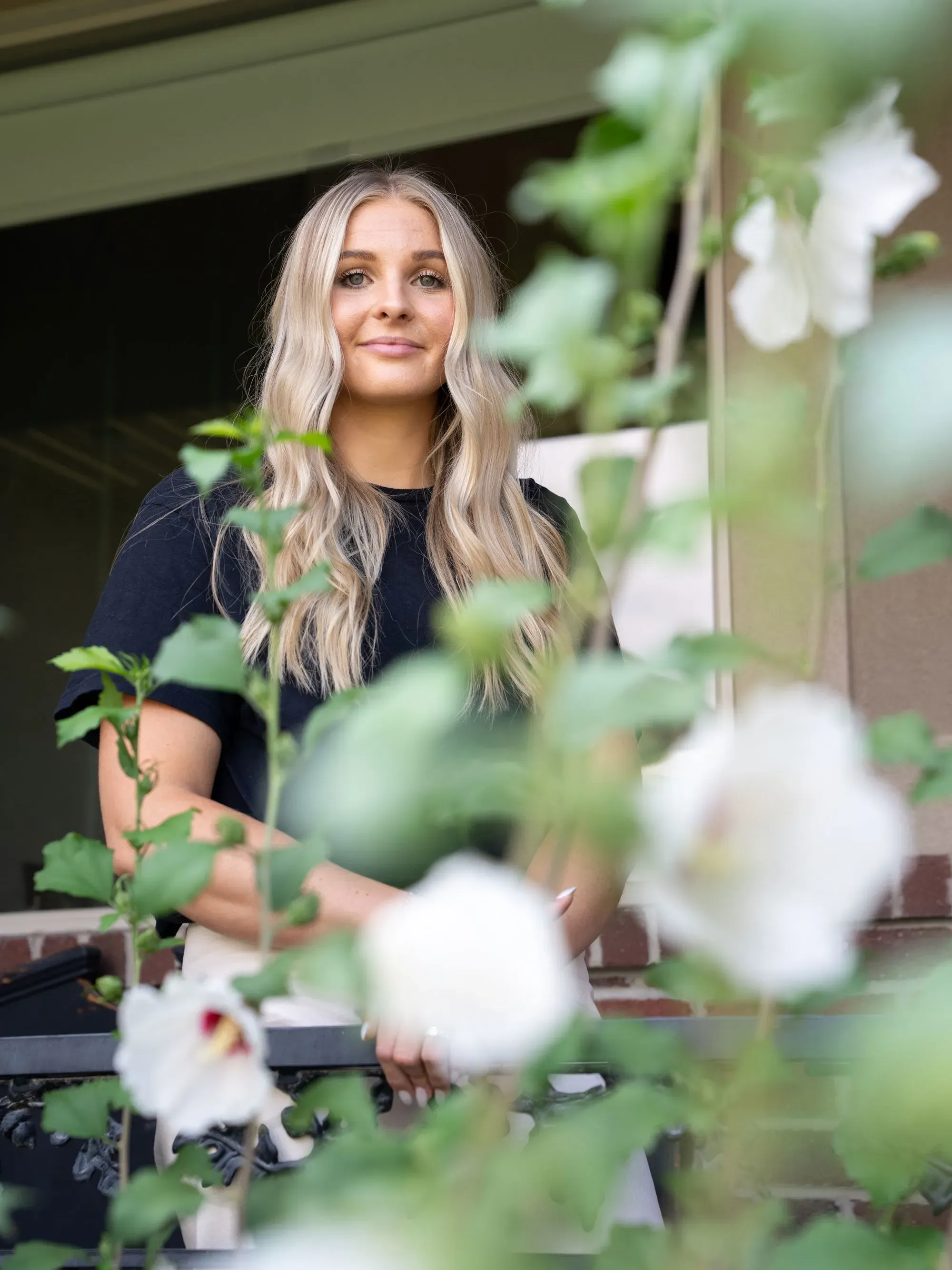 شار أغيلار تقف في فناء منزلها محاطة بأزهار بيضاء، تعكس أسلوب حياتها المزدحم بين التسويق وإدارة أكشاك التصوير في حفلات الزفاف.