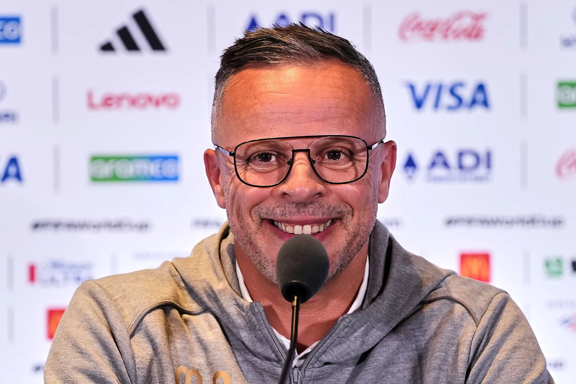 مدرب المغرب محمد وهبي يبتسم خلال مؤتمر صحفي قبيل مباراة ربع نهائي كأس العالم ضد فرنسا، مع شعار كأس العالم وخلفيات رعاة البطولة.