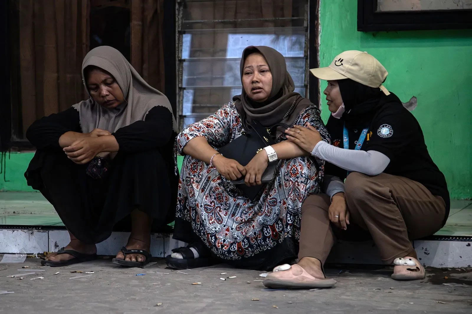 نساء يجلسن في حالة من الحزن والقلق أمام مدرسة منهارة في إندونيسيا، حيث يواصل رجال الإنقاذ البحث عن الطلاب المفقودين.